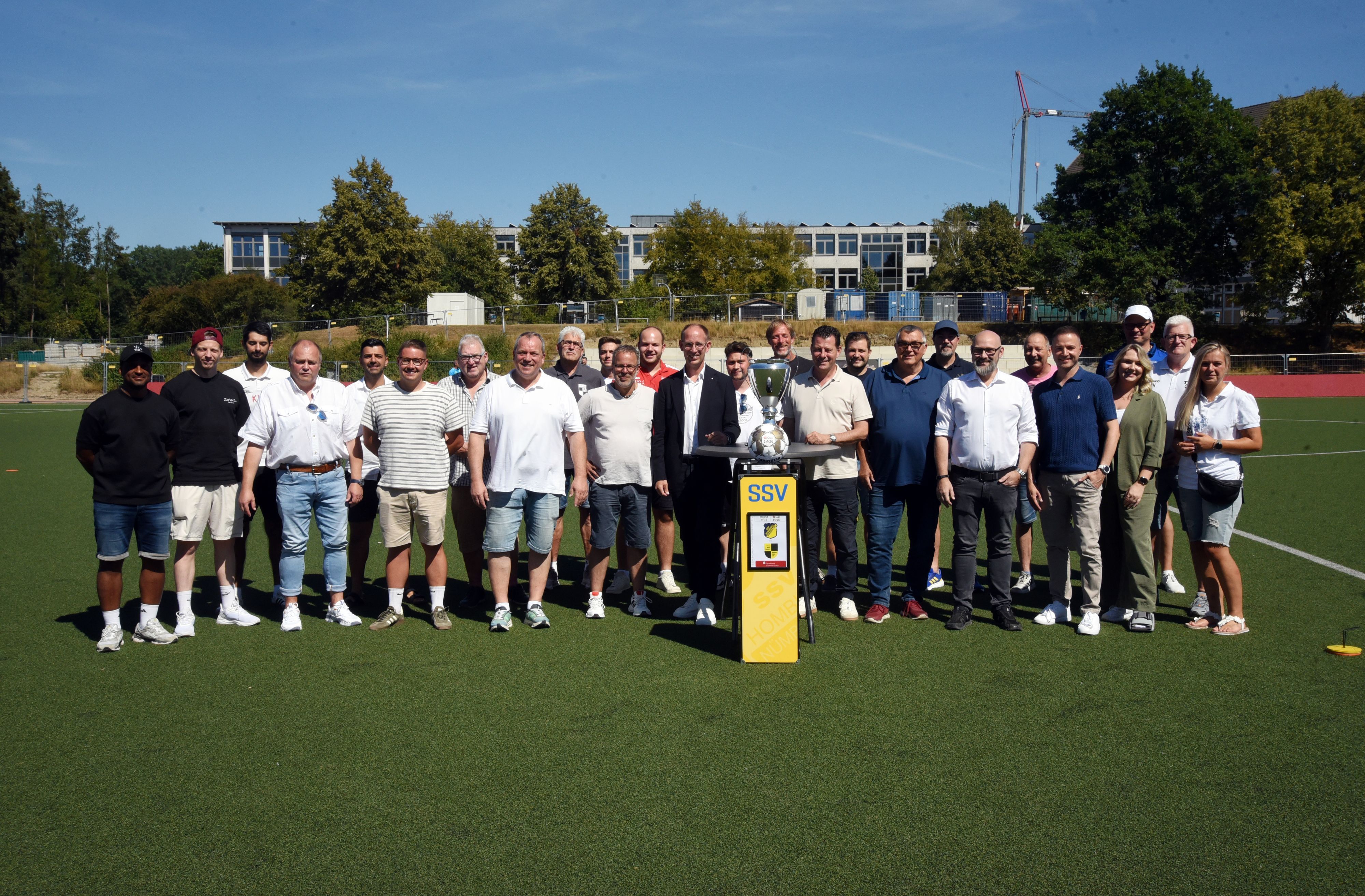 Gruppenfoto aller Verantwortlicher mit dem Pokal in der Mitte.