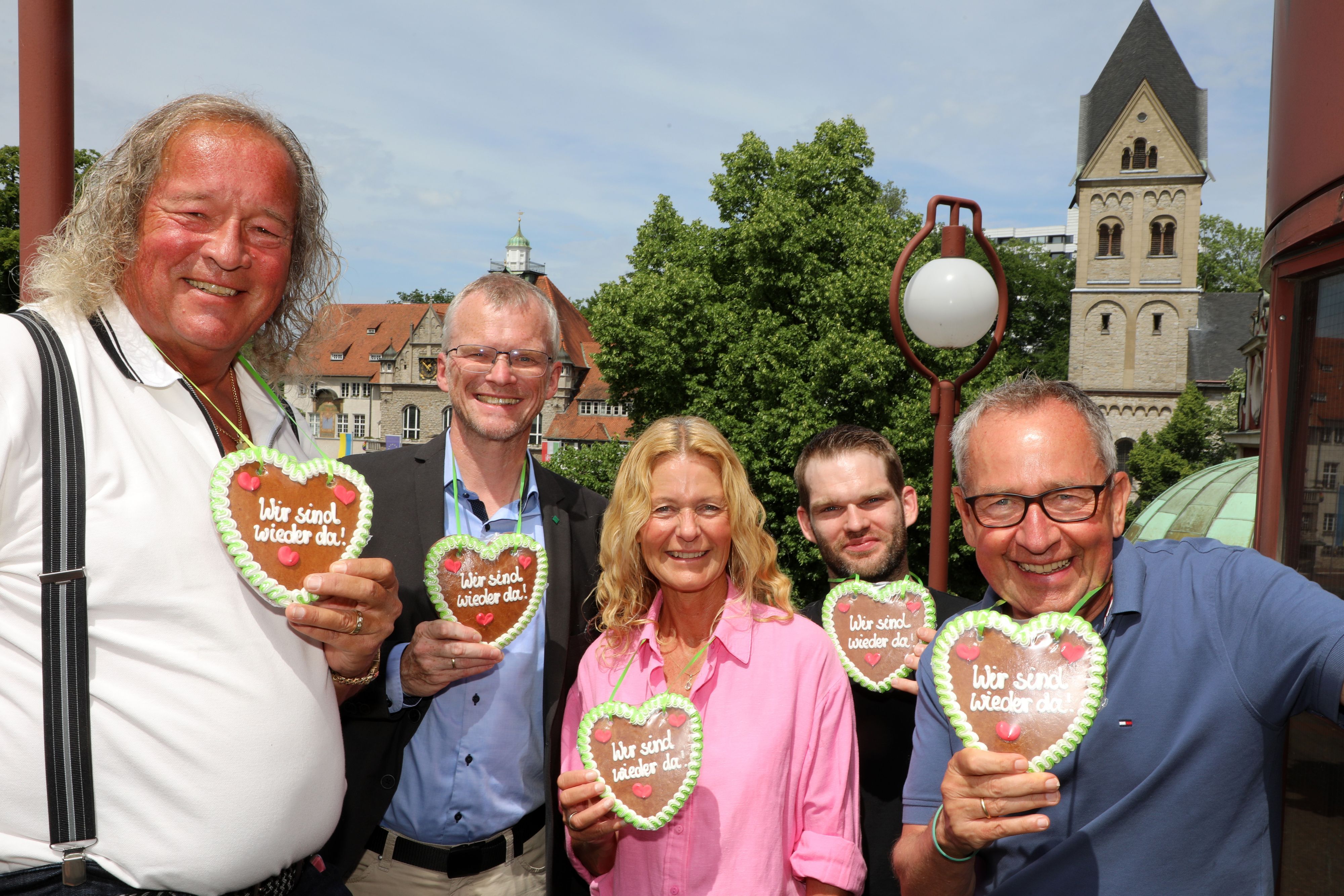 Burkhardt Unrau, Frank Stein, Ute Unrau, Marco Euler und Ferdinand Linzenich stehen mit Lebkuchenherzen mit der Aufschrift „Wir sind wieder da“ auf der Treppe des Bergischen Löwens. Im Hintergrund ist der Konrad-Adenauer-Platz mit Rathaus und Kirche zu sehen.