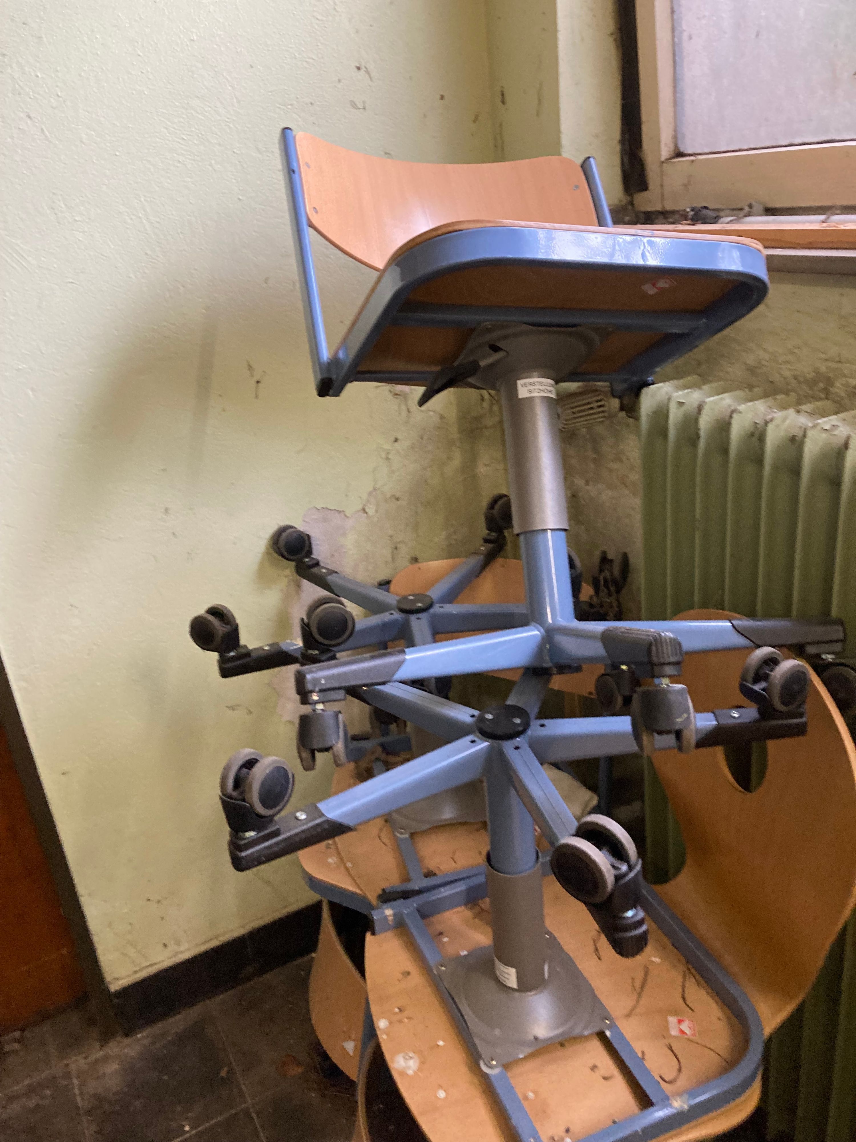 Alte Schulstühle stehen vor einer Wand mit Schimmelbefall.