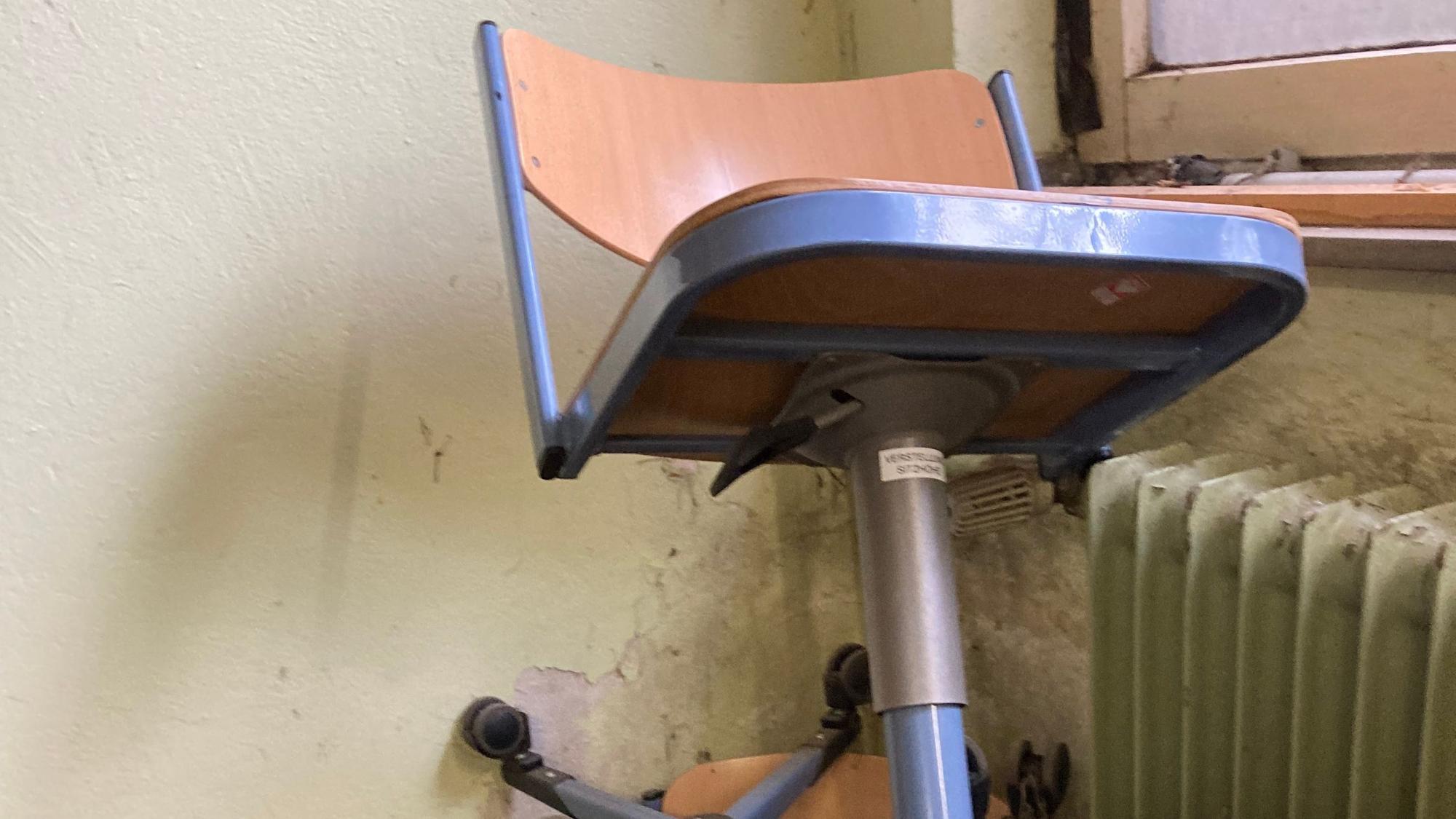 Alte Schulstühle stehen vor einer Wand mit Schimmelbefall.