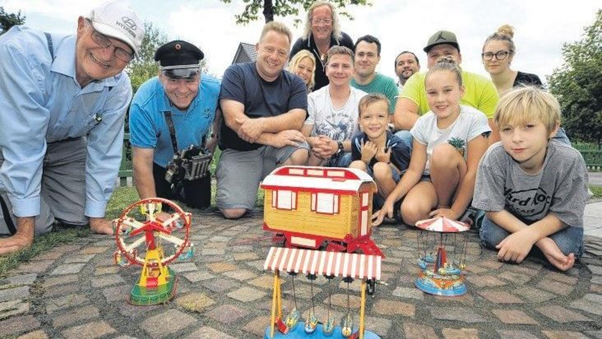 Schausteller und Vertreter der Humanitären Hilfe Overath knien und hocken auf dem privaten „Konrad-Adenauer-Platz“ mit Kirmes von Ute und Burkhardt Unrau in Bergisch Gladbach-Hebborn.