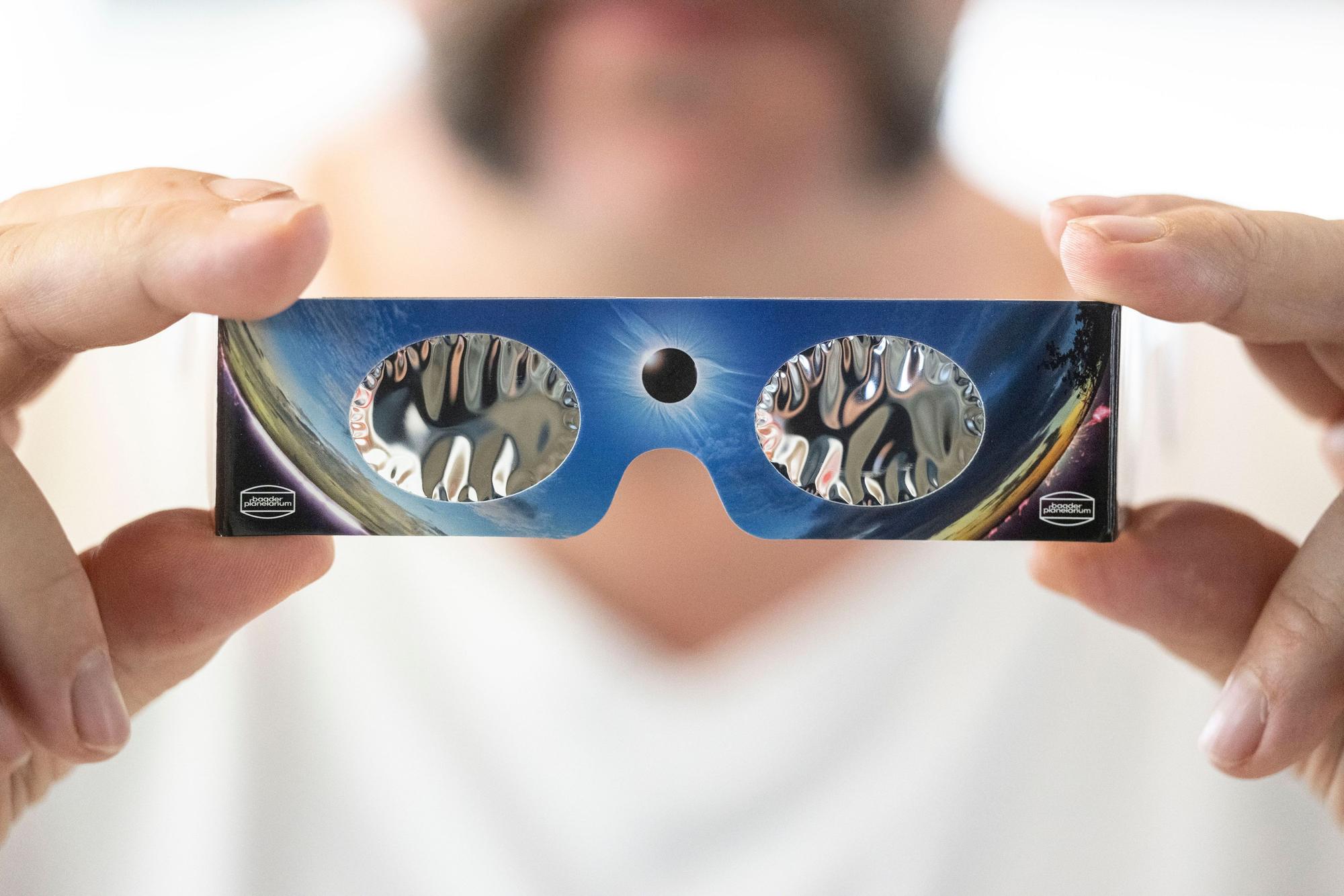 Ein Angestellter hält in einem Fotofachhandelsgeschäft eine Sonnenfinsternis-Brille in der Hand.