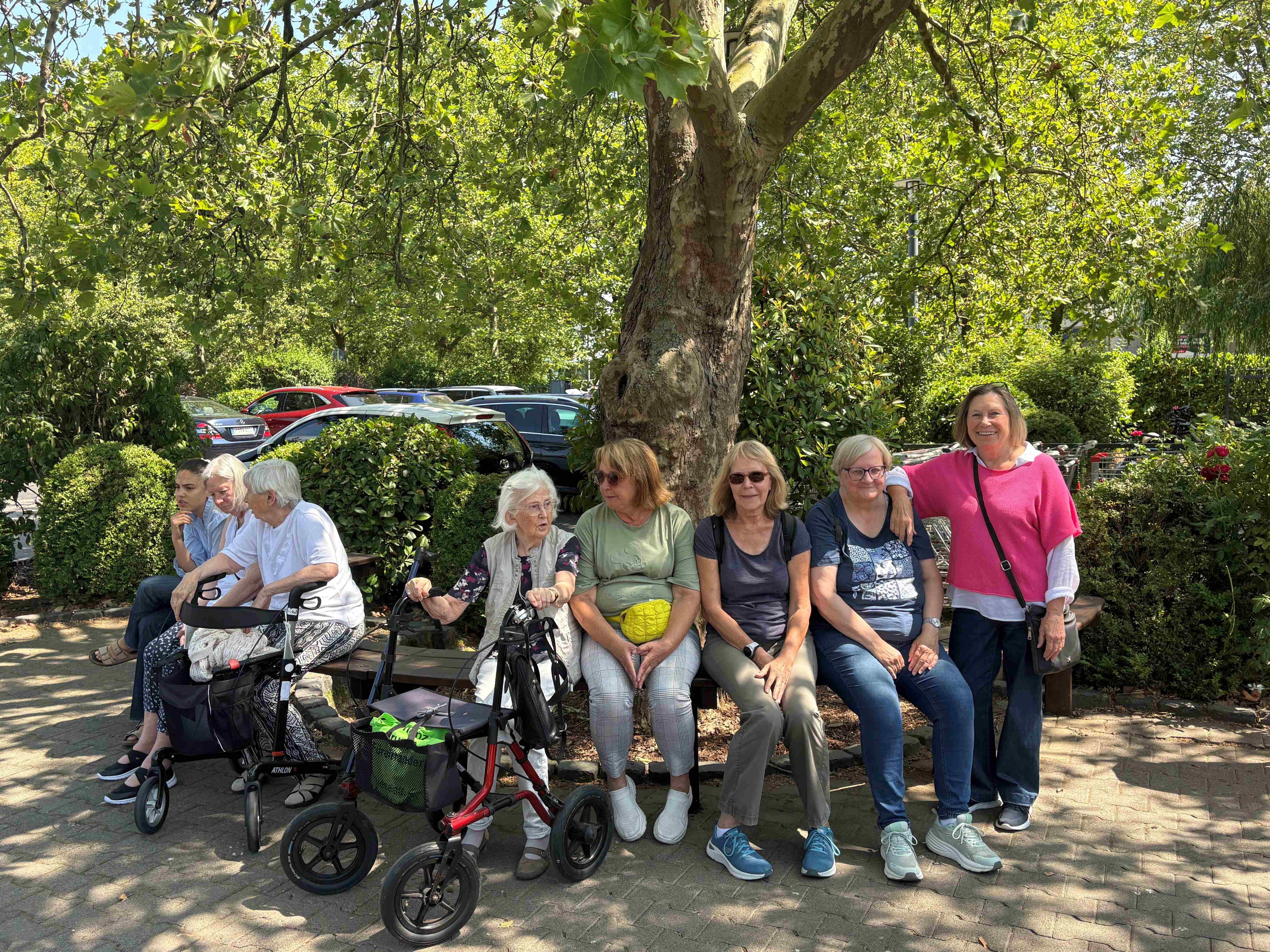 Eine Besuchergruppe sitzt auf einer Bank im Streichelzoo. Manche haben einen Rollator dabei.