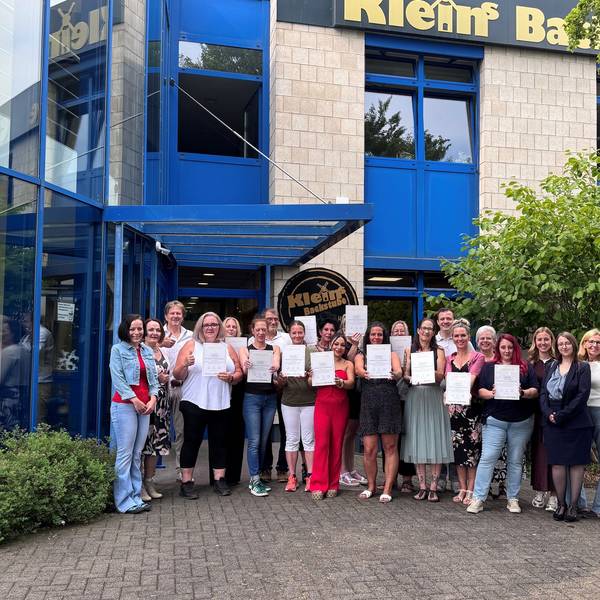 Das Foto zeigt die Absolventinnen mit Urkunden sowie Gratulanten vor der Firmenzentale von „Klein's Backstube“ in Hürth.