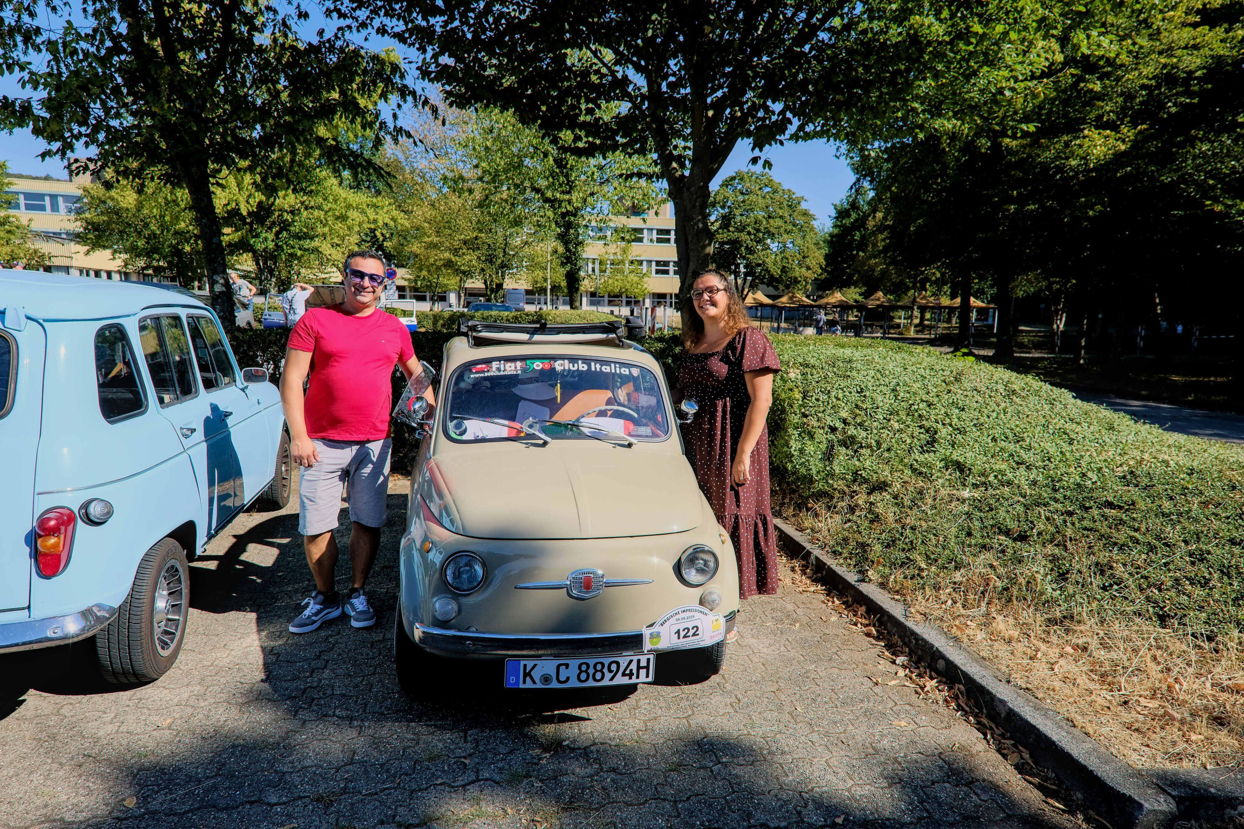 Ein Mann und eine Frau stehen neben einem beigen Fiat 500 110F.