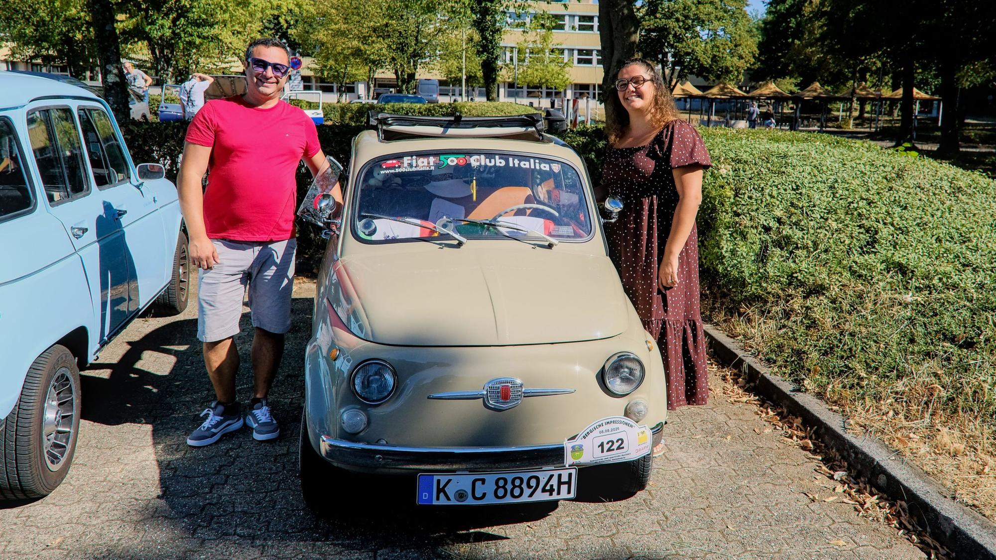 Ein Mann und eine Frau stehen neben einem beigen Fiat 500 110F.