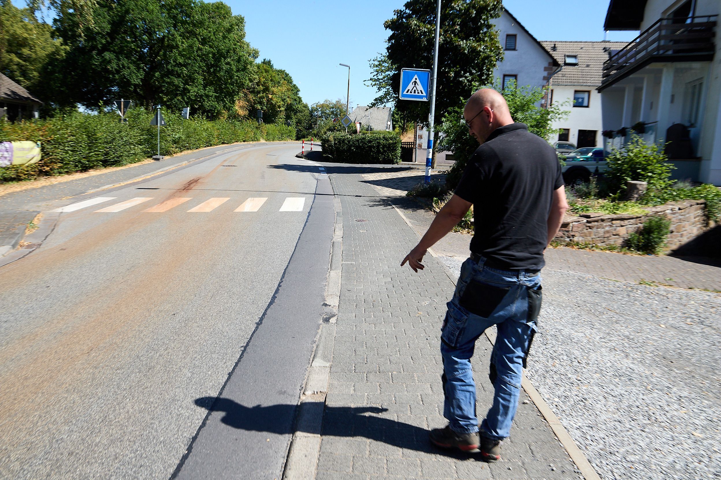 Michael Bröders ist von hinten zu sehen. Er zeigt auf abgefahrene Kanten zwischen der Straße und seinem Grundstück in Marmagen.