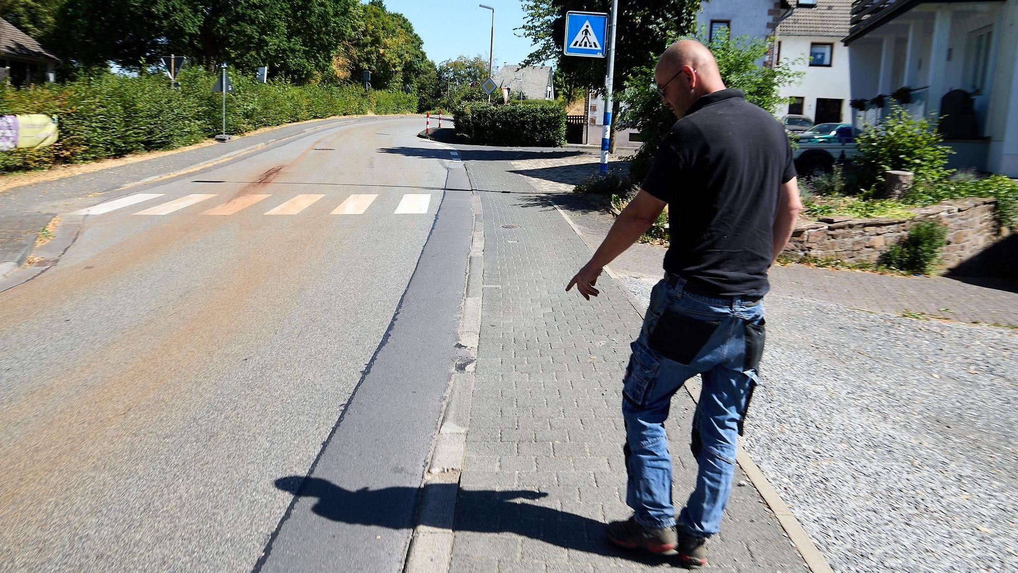 Michael Bröders ist von hinten zu sehen. Er zeigt auf abgefahrene Kanten zwischen der Straße und seinem Grundstück in Marmagen.