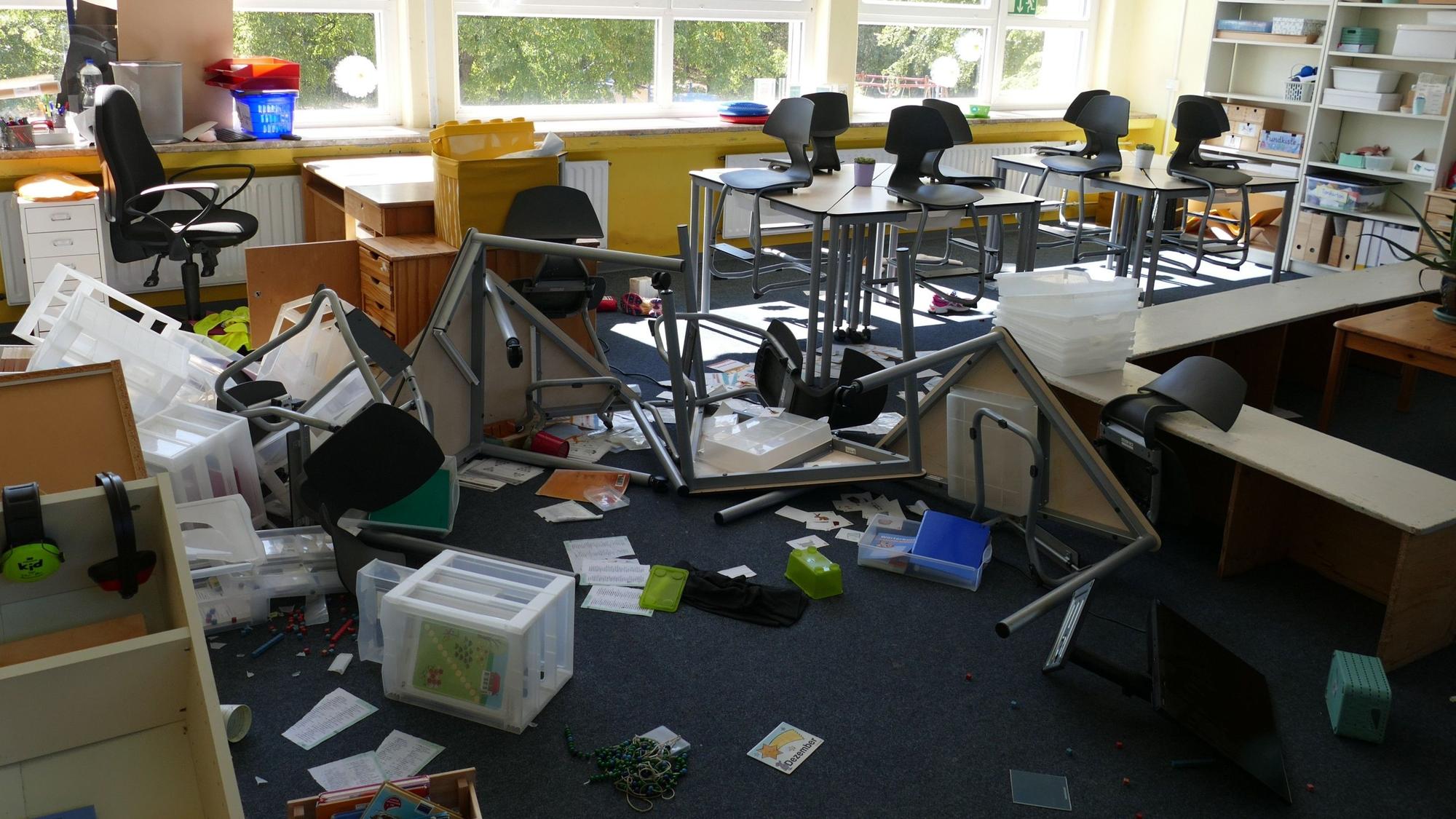 EIn Klassenzimmer in einer Grundschule. Stühle und Tische sind umgeworfen, der Inhalt von Regalen liegt auf dem Bodeni.