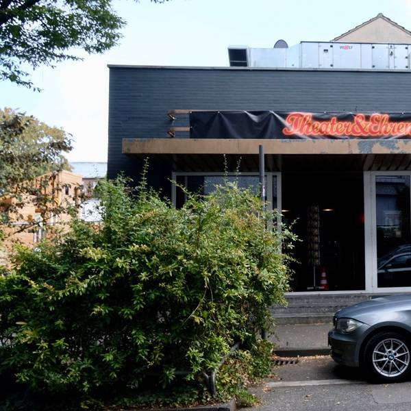 Ein flaches Gebäude ist zu sehen. Auf einem Transparent über dem Eingang steht Theater & Ehrenfeld.