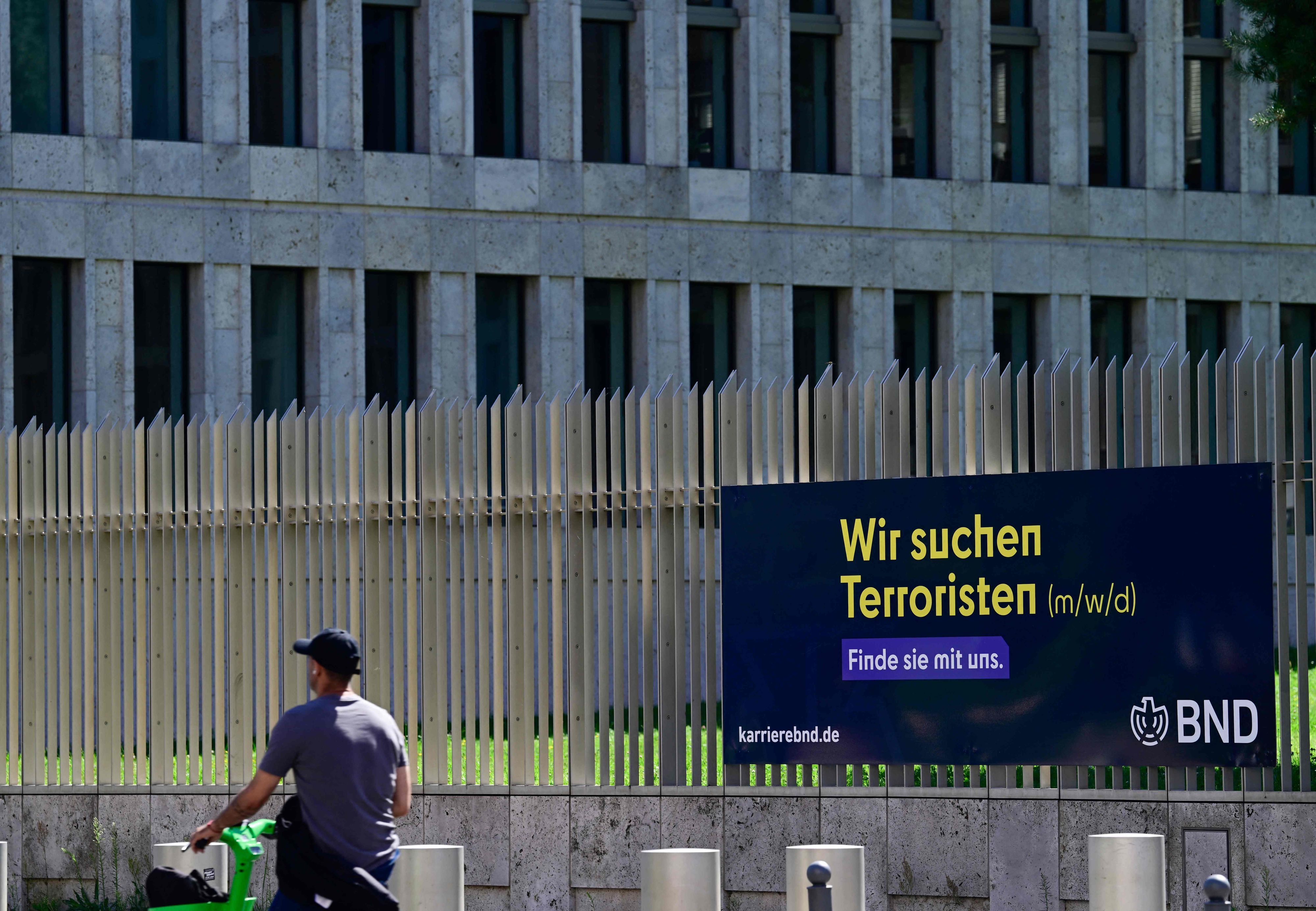 Ein Mann geht in Berlin an einer Stellenanzeige mit der Aufschrift „Wir suchen Terroristen“ vorbei, die am Zaun rund um die Zentrale des Bundesnachrichtendienstes (BND) angebracht ist. Die deutsche Regierung hat einer umfassenden Reform der Nachrichtendienste des Landes zugestimmt. Diese sollen weitreichende neue Befugnisse für verdeckte Operationen und Maßnahmen gegen Bedrohungen aus dem Ausland erhalten.
