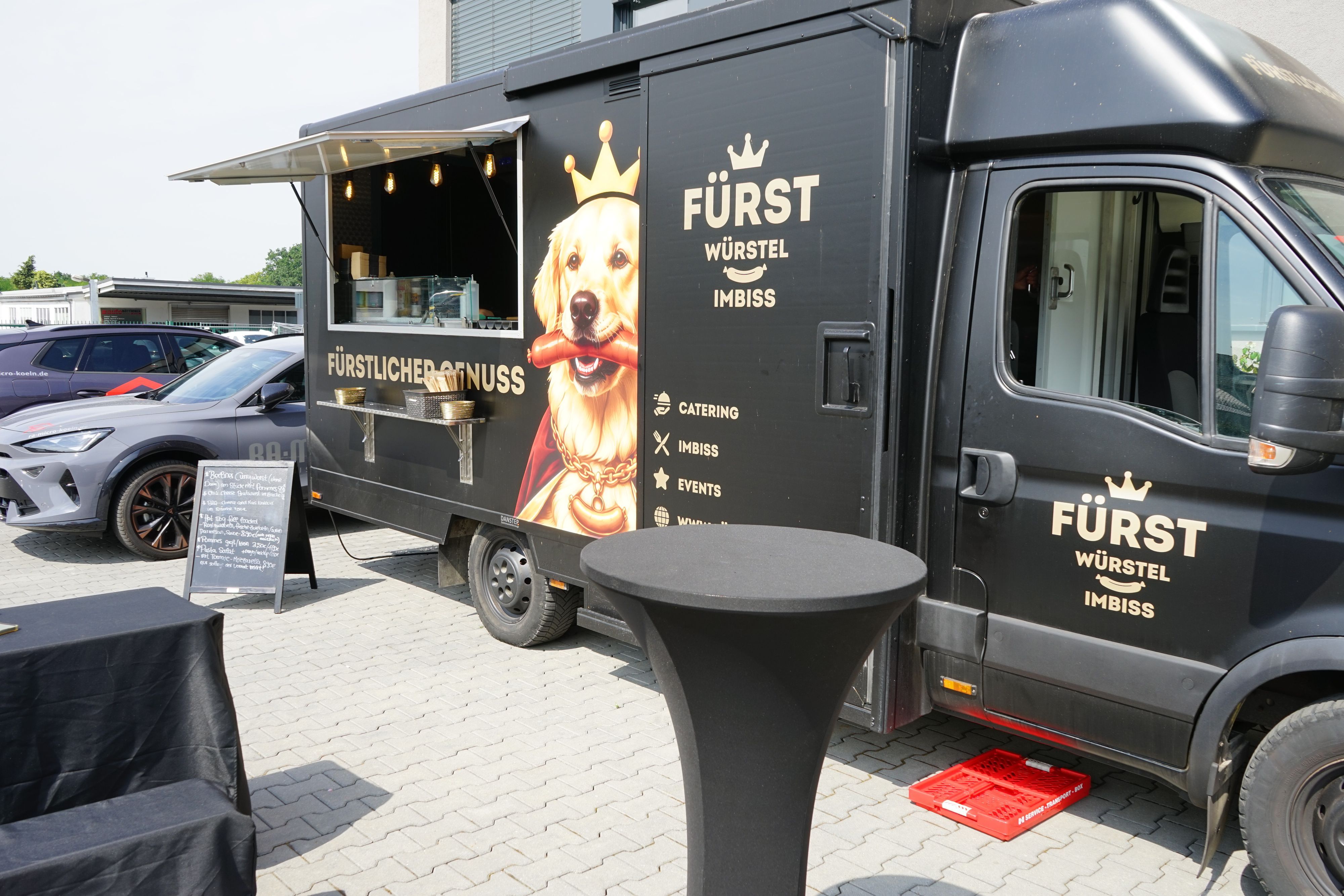 Zu sehen ist ein schwarzer Foodtruck mit einem KI-generierten Bild von einem Hund mit Wurst und Krone darauf.
