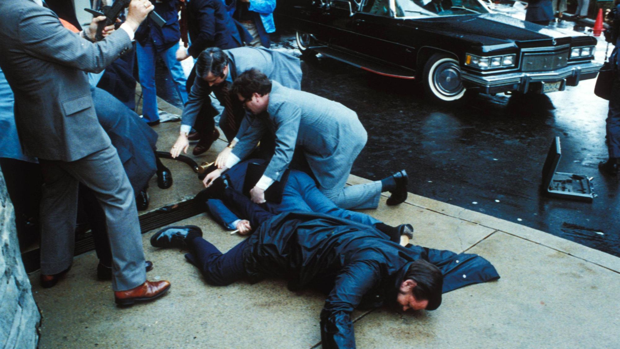 Unmittelbar nach den Schüssen auf US-Präsident Ronald Reagan überwältigen Sicherheitskräfte den Attentäter John Hinckley Jr. vor dem Washington Hilton Hotel, während der schwer verletzte Regierungssprecher James Brady und ein Polizist am Boden liegen.