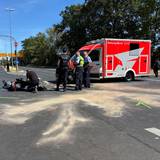 Vor einem RTW liegt ein Motorrad auf der Fahrbahn, Polizisten stehen davor, einer kniet.