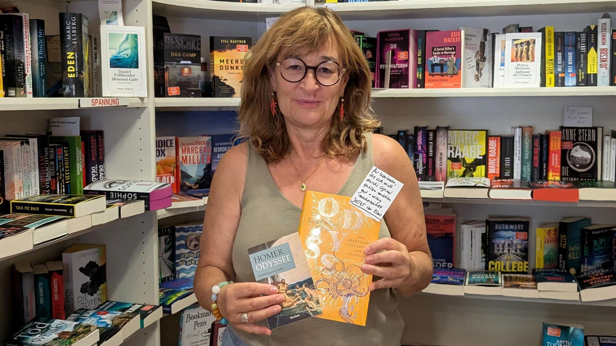Buchhändlerin Renate Elsen steht mit zwei Büchern vor einem Regal.