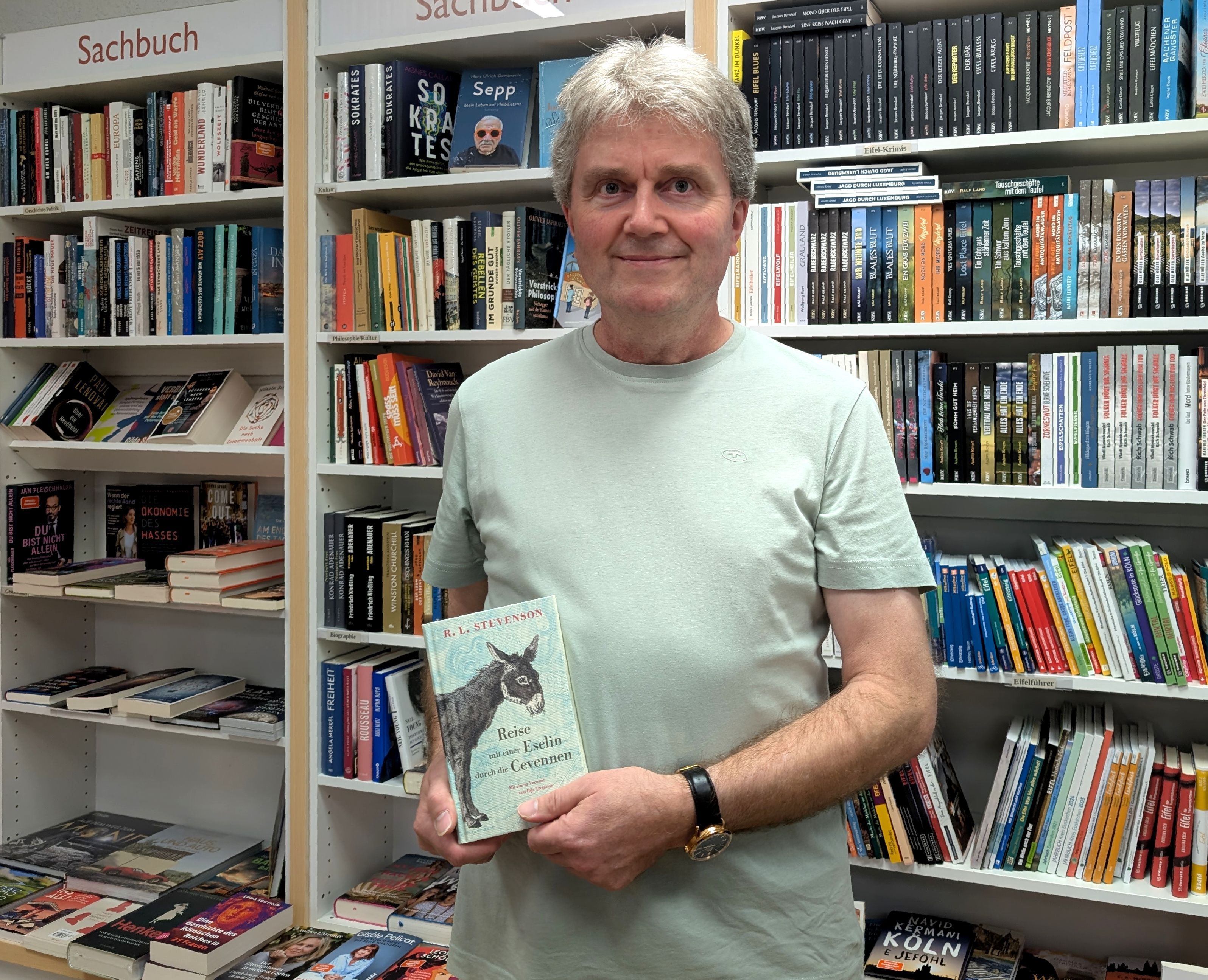 Buchhändler Thomas Pavlik mit seiner Leseempfeehlung vor einem Büccherregal.