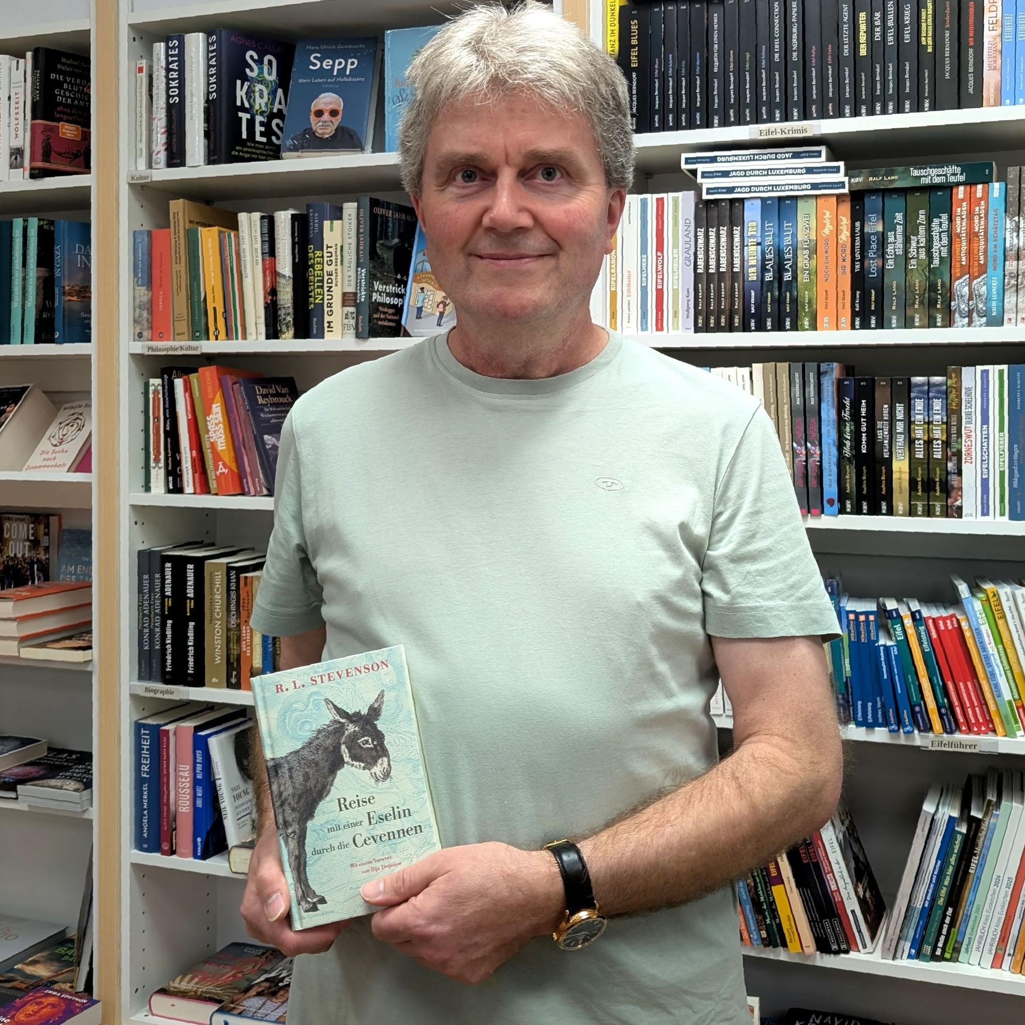 Buchhändler Thomas Pavlik mit seiner Leseempfeehlung vor einem Büccherregal.