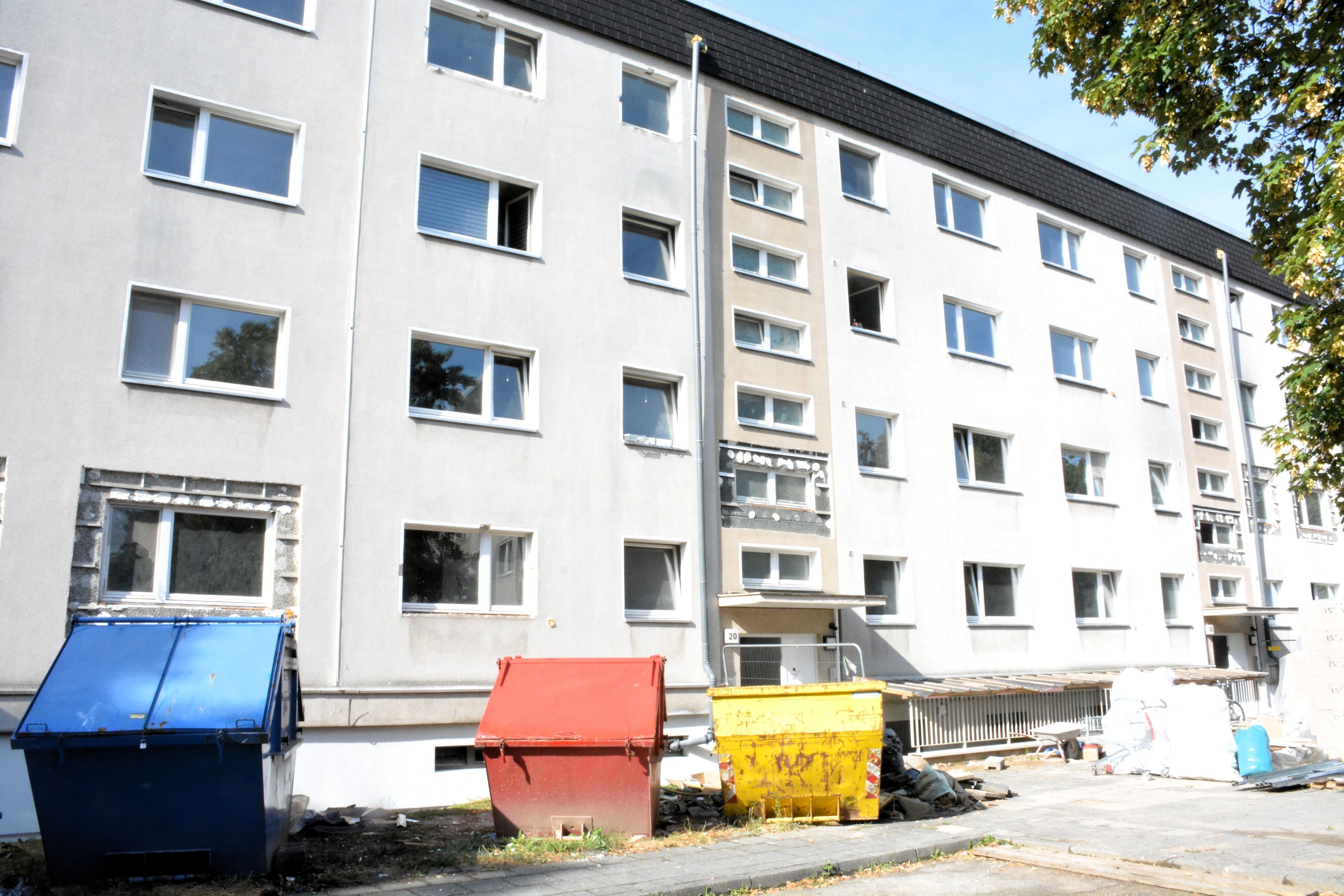 Bunte Baucontainer stehen vor einem viergeschossigen Haus.