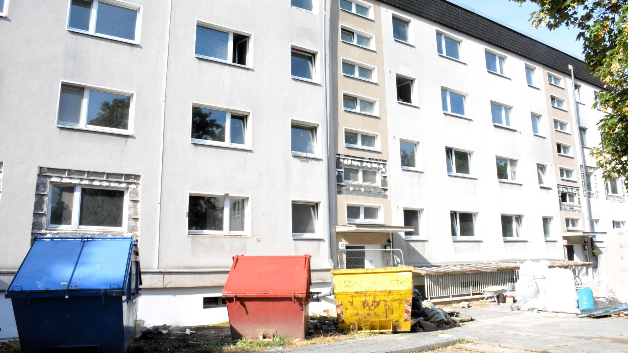 Bunte Baucontainer stehen vor einem viergeschossigen Haus.