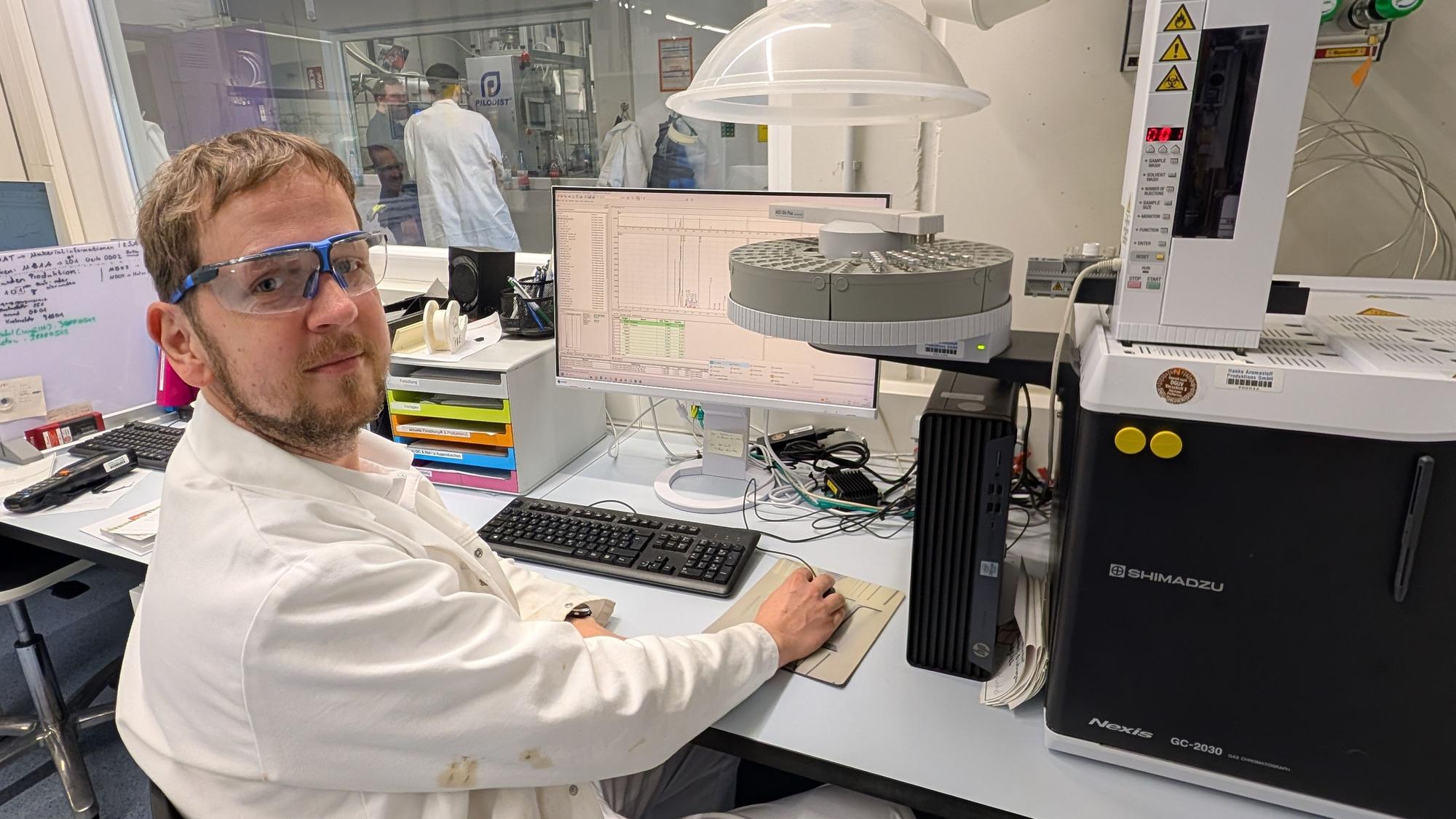 Das Foto zeigt den Chemiker vor dem Computer und einem Analysegerät.
