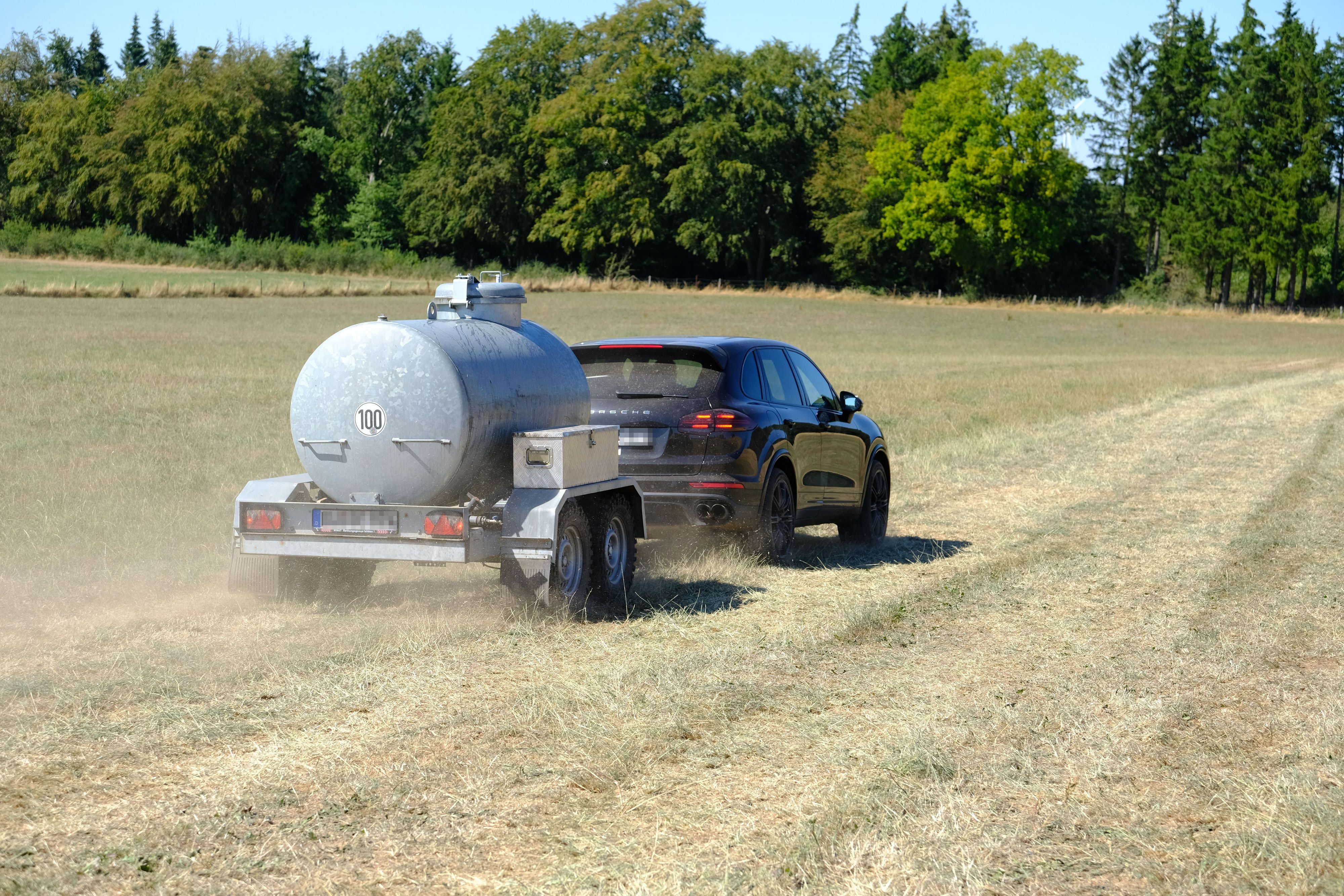 Ein Auto zieht einen Anhänger, in dem Wasser zur Einsatzstelle transportiert wird.