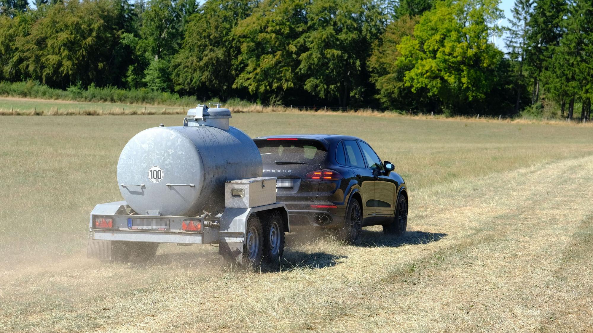 Ein Auto zieht einen Anhänger, in dem Wasser zur Einsatzstelle transportiert wird.