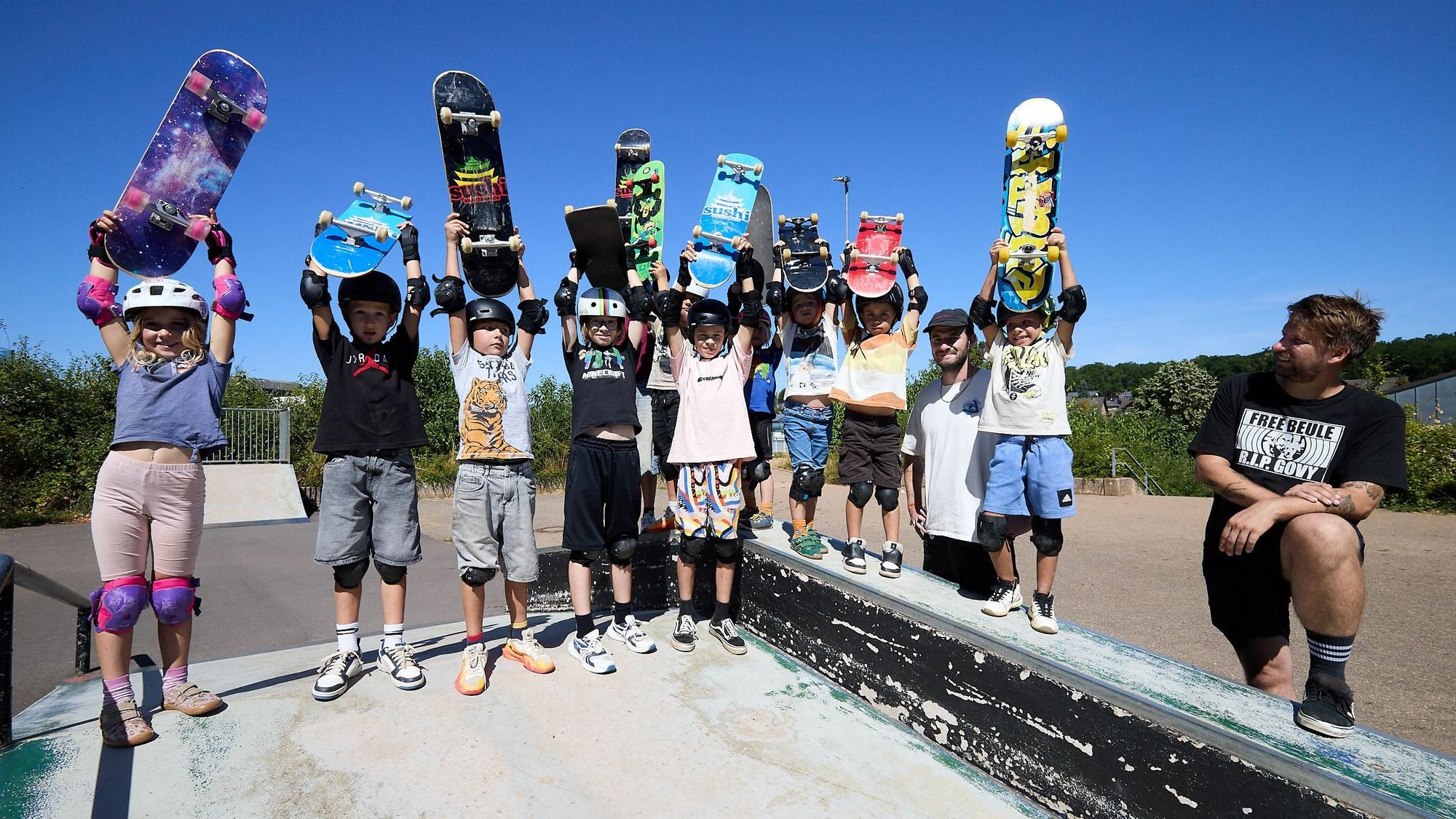Zehn Kinder halten ihre Skateboards in den Himmel. Zwei Männer schauen zu.