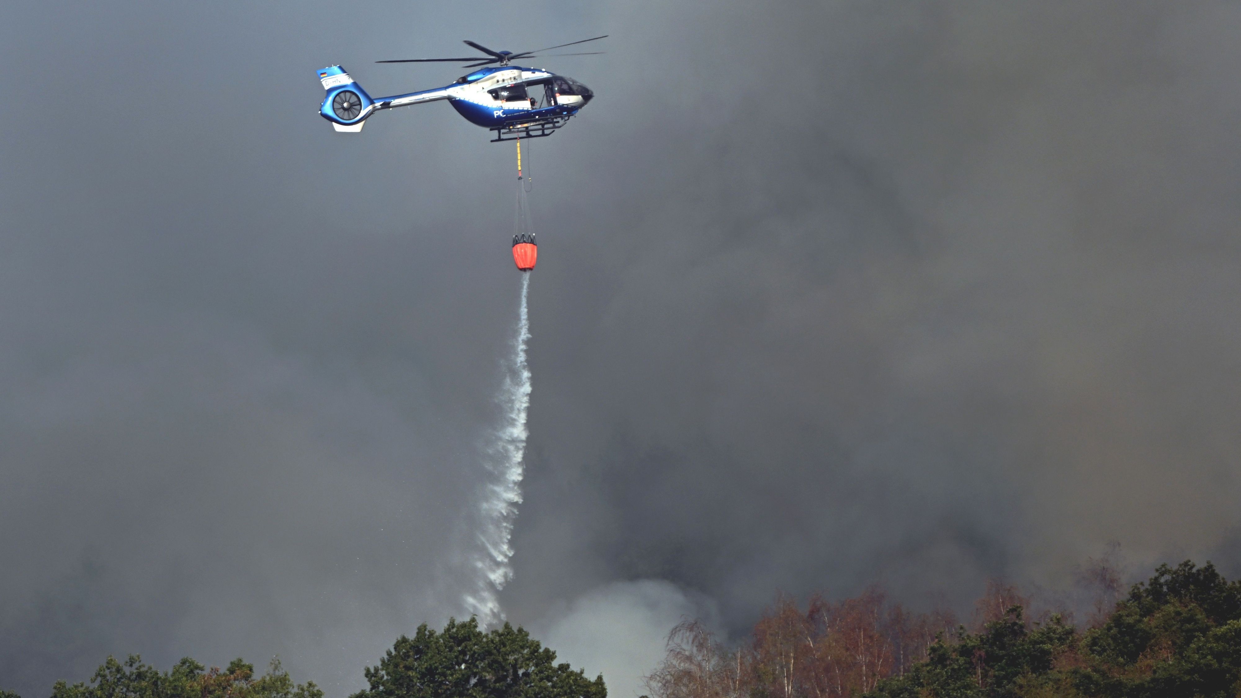 Ein Polizeihubschrauber mit Löschwasser-Außenlastbehälter unterstützt die Löscharbeiten beim Waldbrand im Hürtgenwald.
