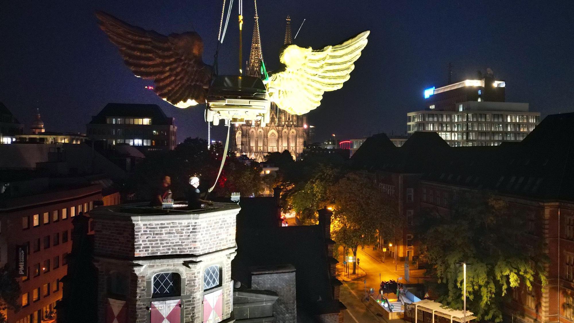 13.08.2026, Nordrhein-Westfalen, Köln: Das goldene Flügelauto des Kölner Künstlers HA Schult wird von einem Kran vom Turm des historischen Zeughauses gehoben, weil das Gebäude baufällig ist. Foto: Federico Gambarini/dpa +++ dpa-Bildfunk +++