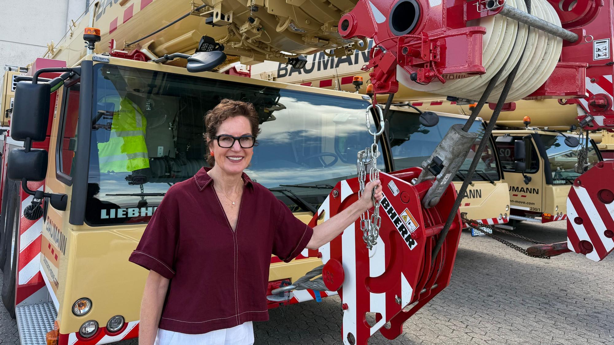 Sabine Baumann steht vor einem ihrer gewaltigen Liebherr Mobilkräne.