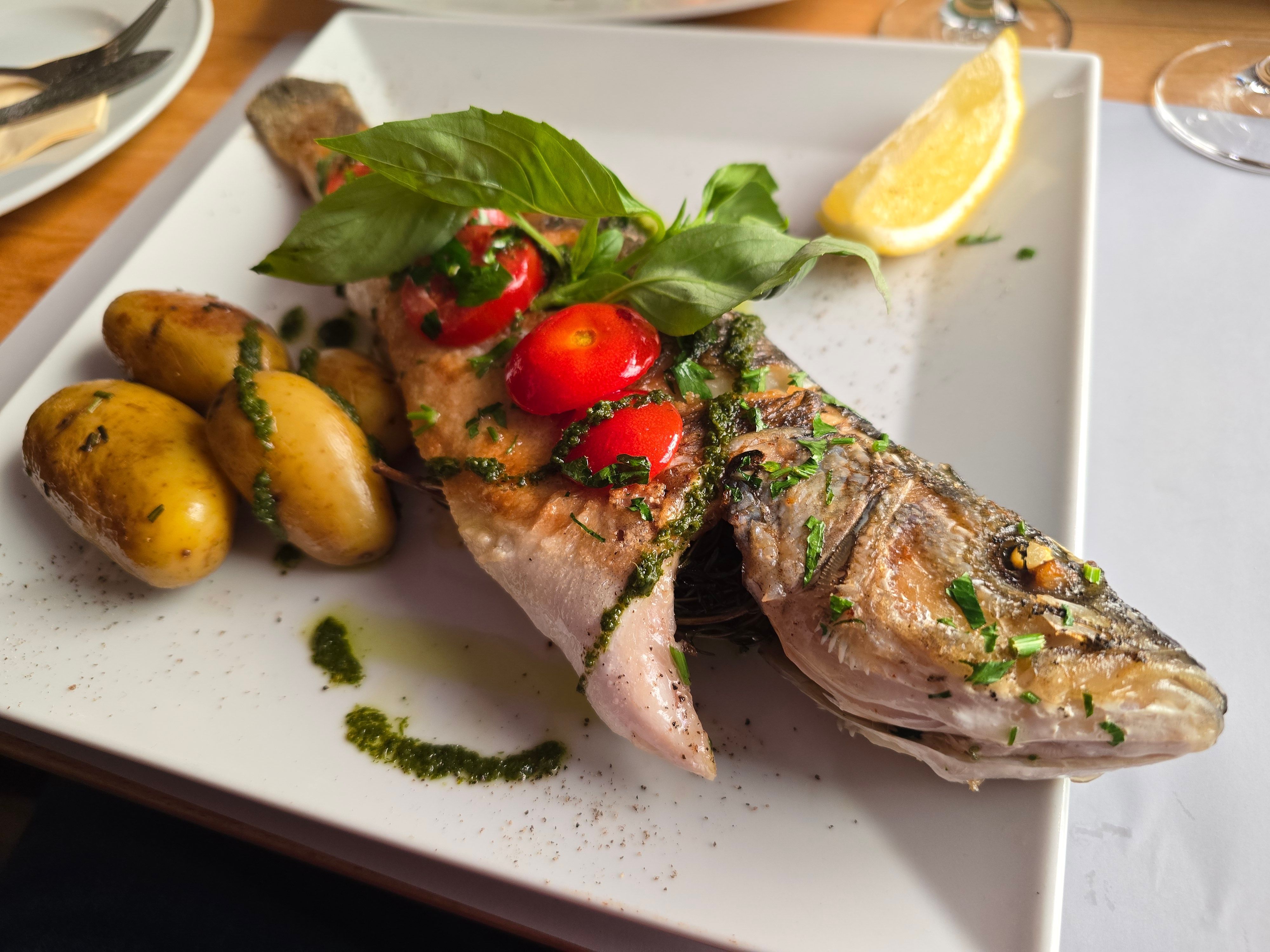 Fisch garniert mit Pesto, Tomaten und Basilikum. Anbei Kartoffeln.