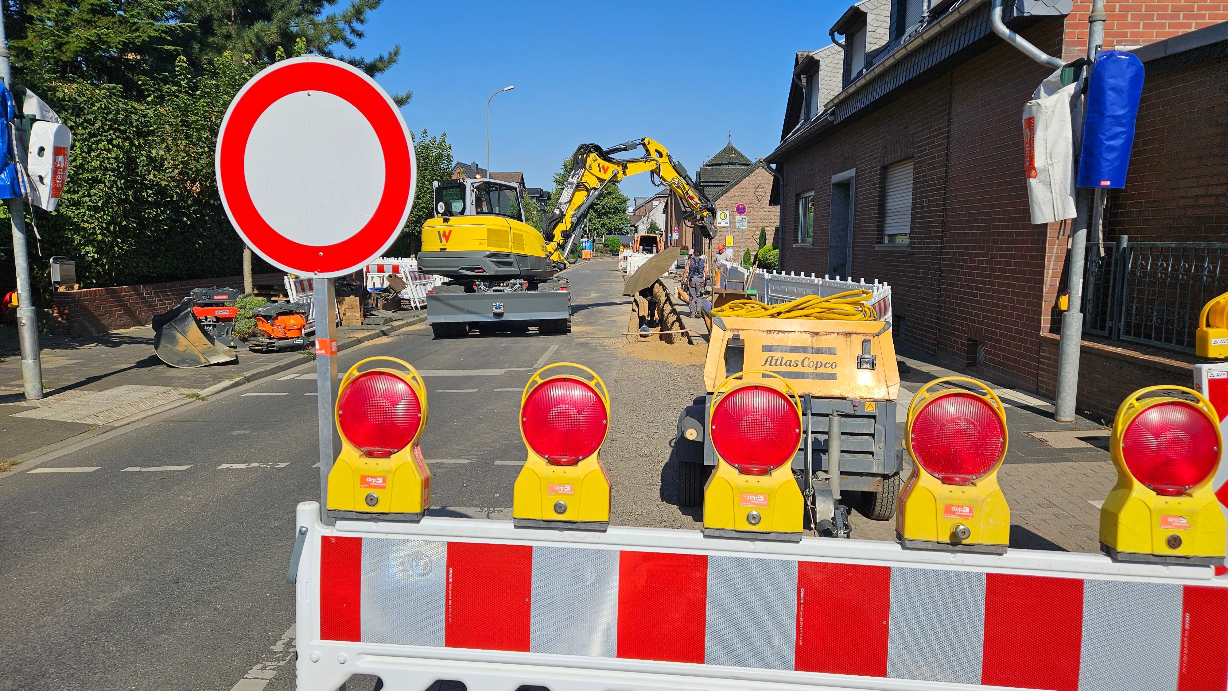 Zu sehen ist eine Baustelle auf einer Straße mit Absperrungen und einem Bagger.