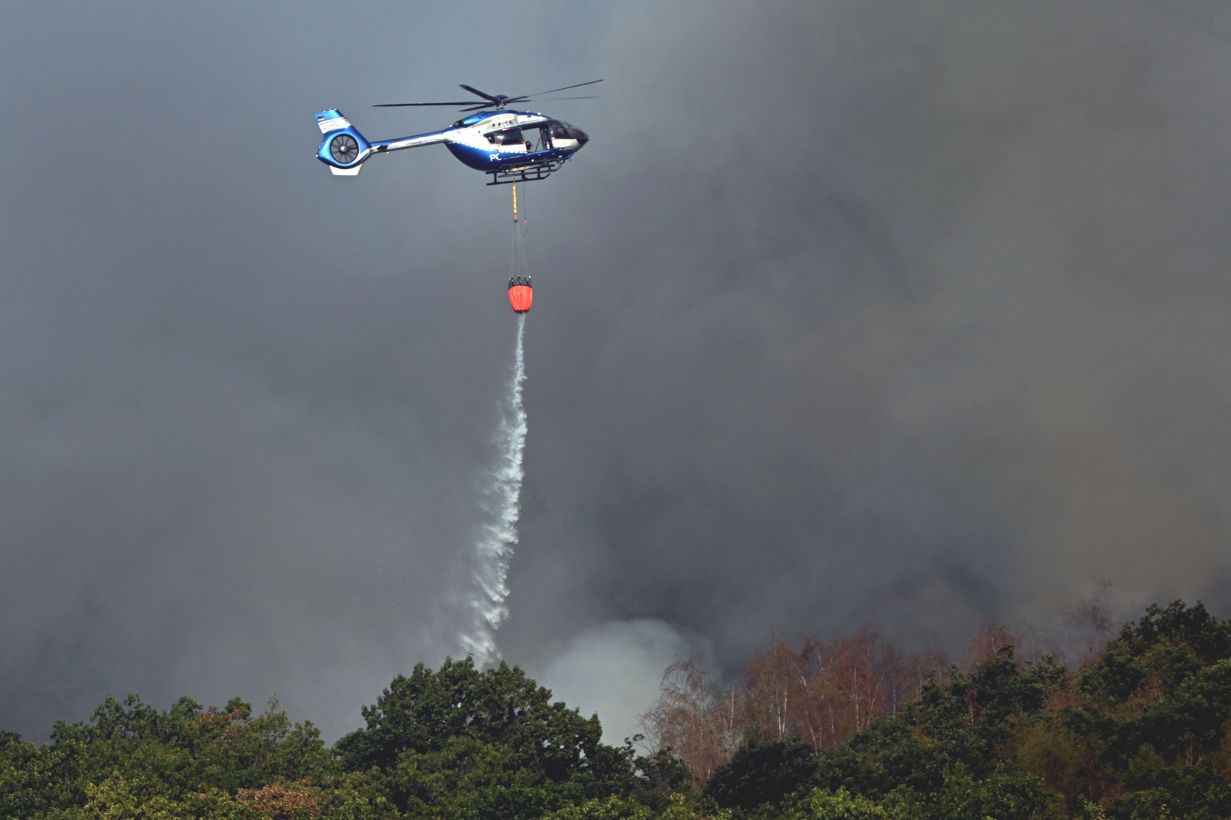 Ein Polizeihubschrauber mit Löschwasser-Außenlastbehälter unterstützt die Löscharbeiten beim Waldbrand im Hürtgenwald.