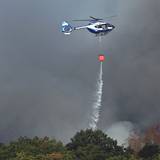Ein Polizeihubschrauber mit Löschwasser-Außenlastbehälter unterstützt die Löscharbeiten beim Waldbrand im Hürtgenwald.