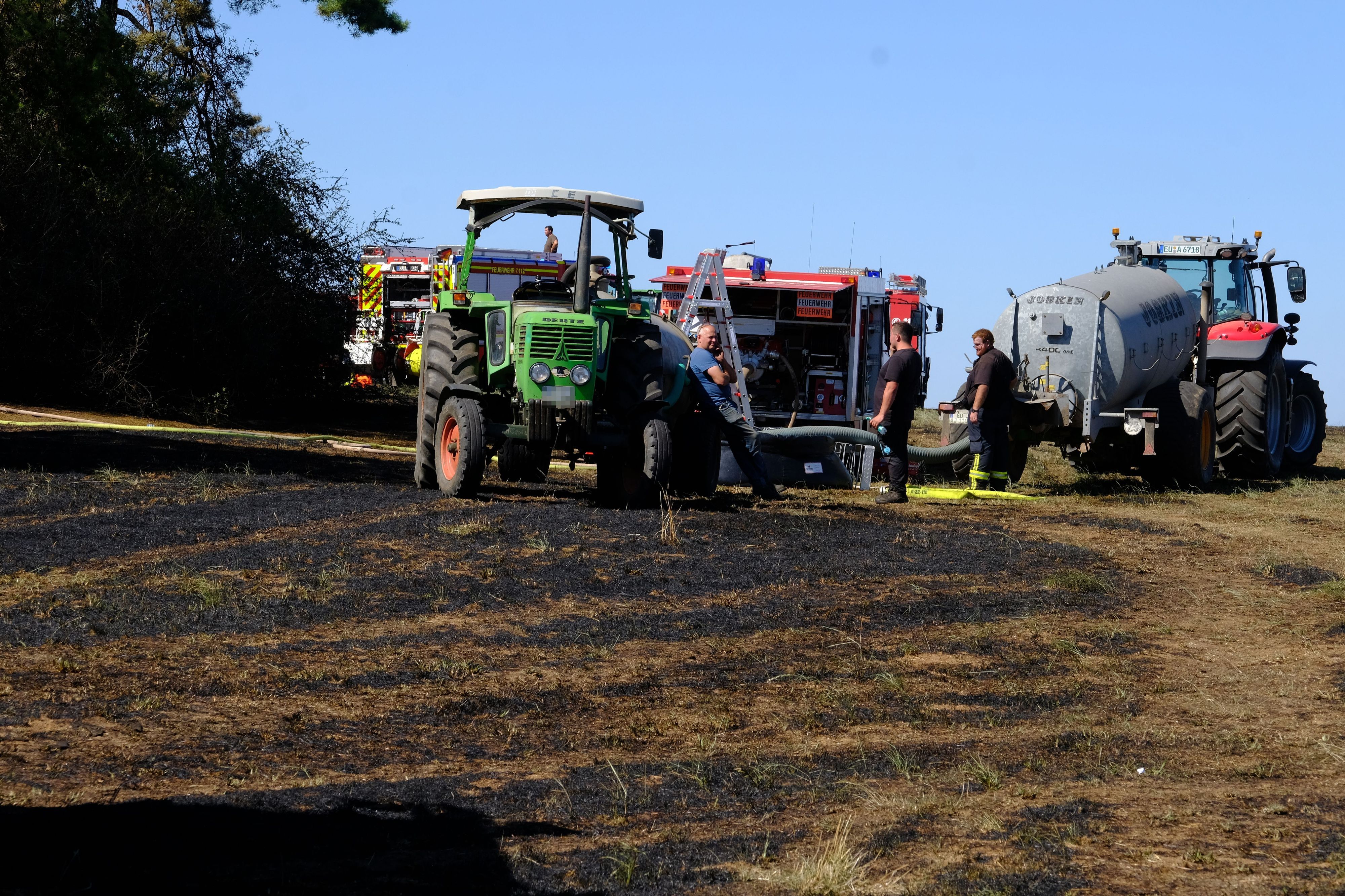 Trecker und Feuerwehrfahrzeuge stehen auf einem Feld.