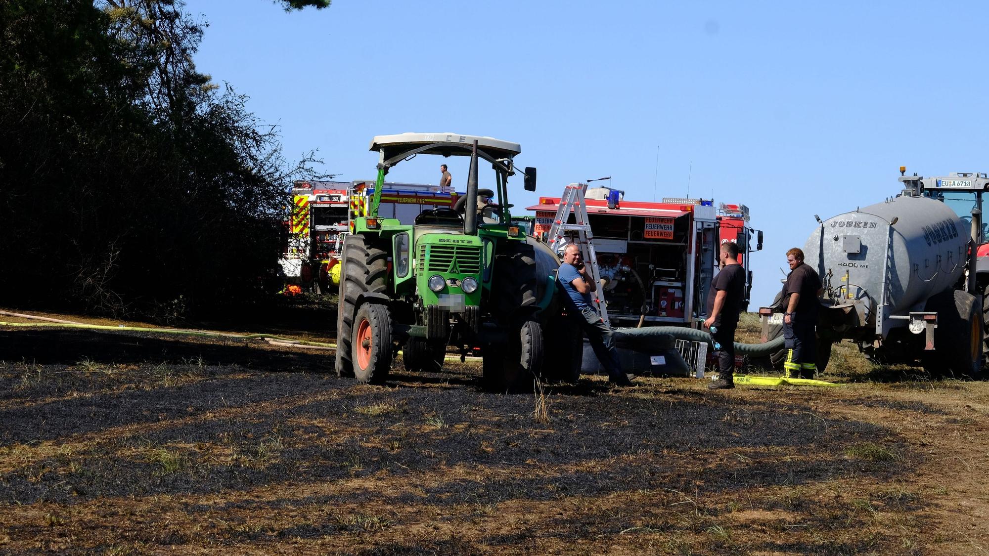 Trecker und Feuerwehrfahrzeuge stehen auf einem Feld.