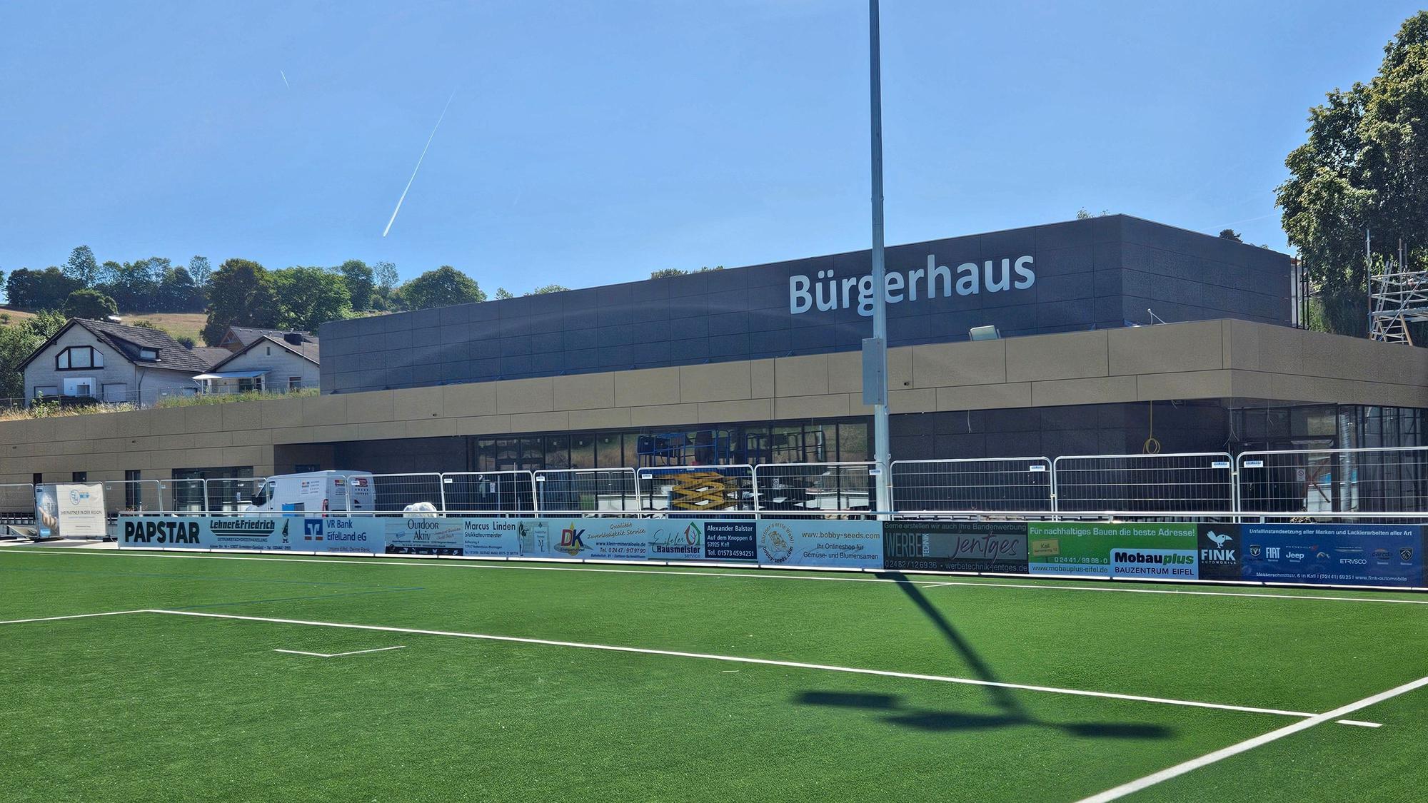 Blick auf einen Teil des Sportplatzes und das im Bau befindliche Bürgerhaus.