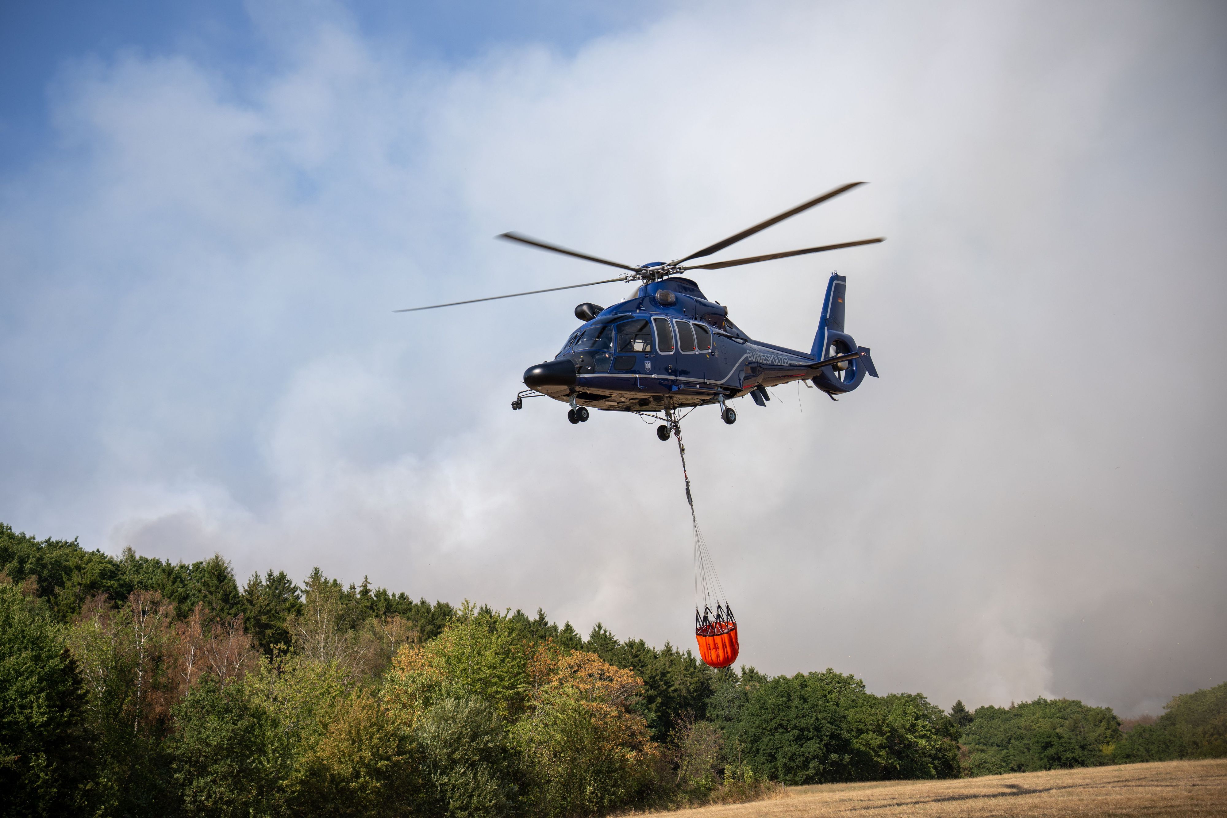 Ein Helikopter der Bundespolizei mit einem Löschwasser-Außenlastbehälter ist beim Waldbrand im Hürtgenwald im Einsatz.