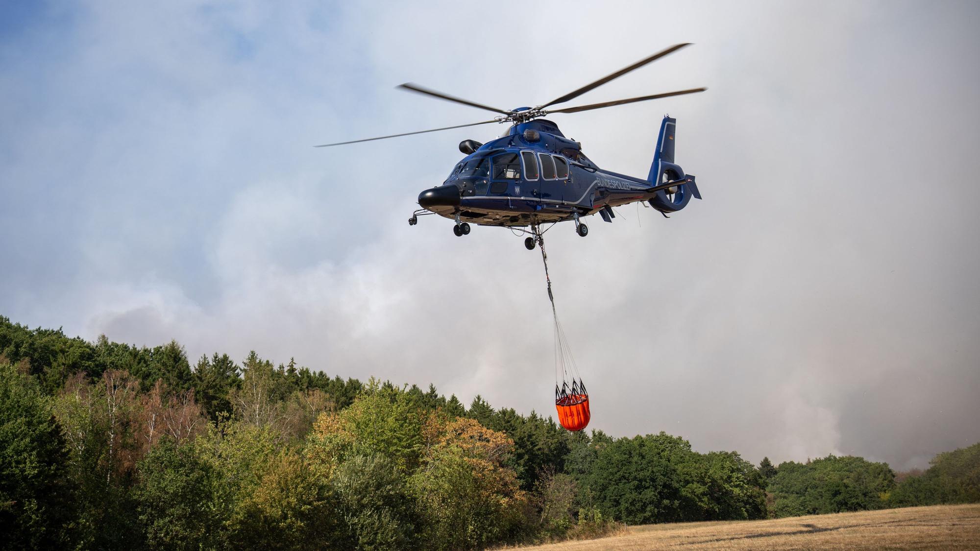 Ein Helikopter der Bundespolizei mit einem Löschwasser-Außenlastbehälter ist beim Waldbrand im Hürtgenwald im Einsatz.