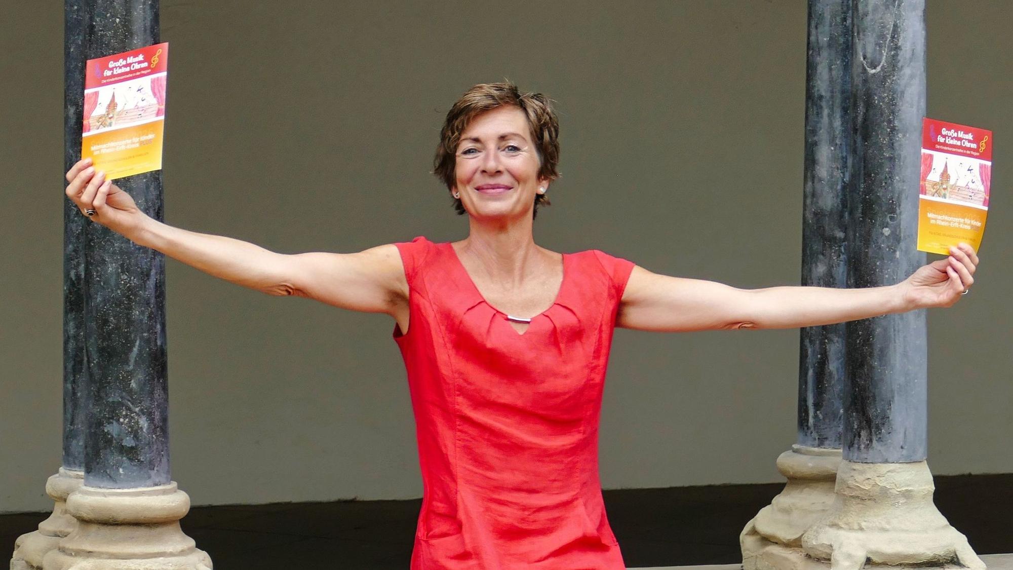 Eine Frau hält zwei Programme in ihren Händen, im Hintergrund sind Säulen zu sehen.