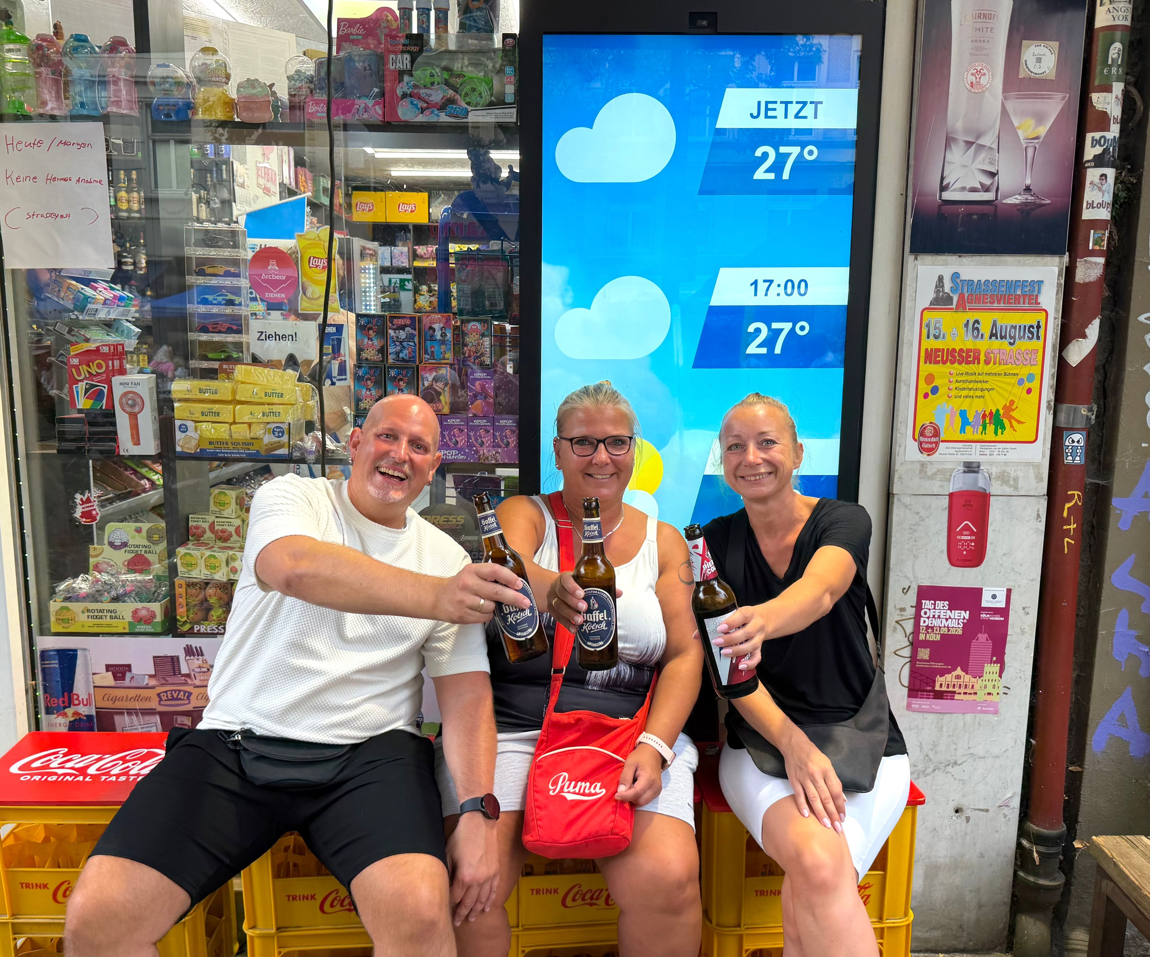 Besucher des Straßenfestes Jupp, Nadine und Jacky sitzen mit Getränken vor einem Kiosk