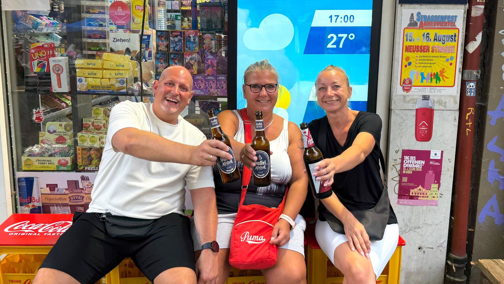 Besucher des Straßenfestes Jupp, Nadine und Jacky sitzen mit Getränken vor einem Kiosk