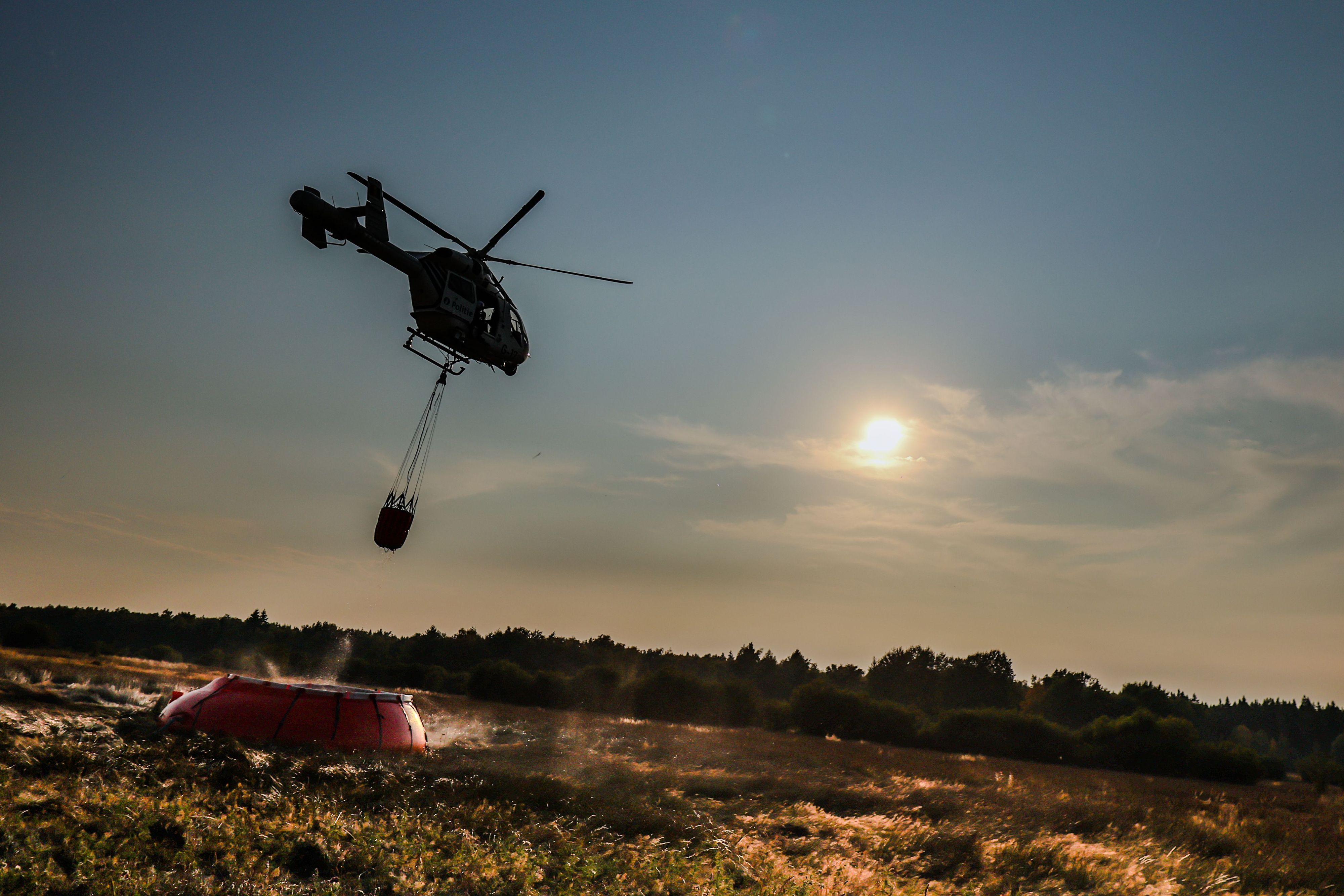 Ein Hubschrauber der belgischen Polizei mit einem Bambi Bucket, ein Löschwasser-Außenlastbehälter, fliegt zu einer provisorischen Wasseraufladestelle im Hohen Venn, um Löschwasser aufzutanken.