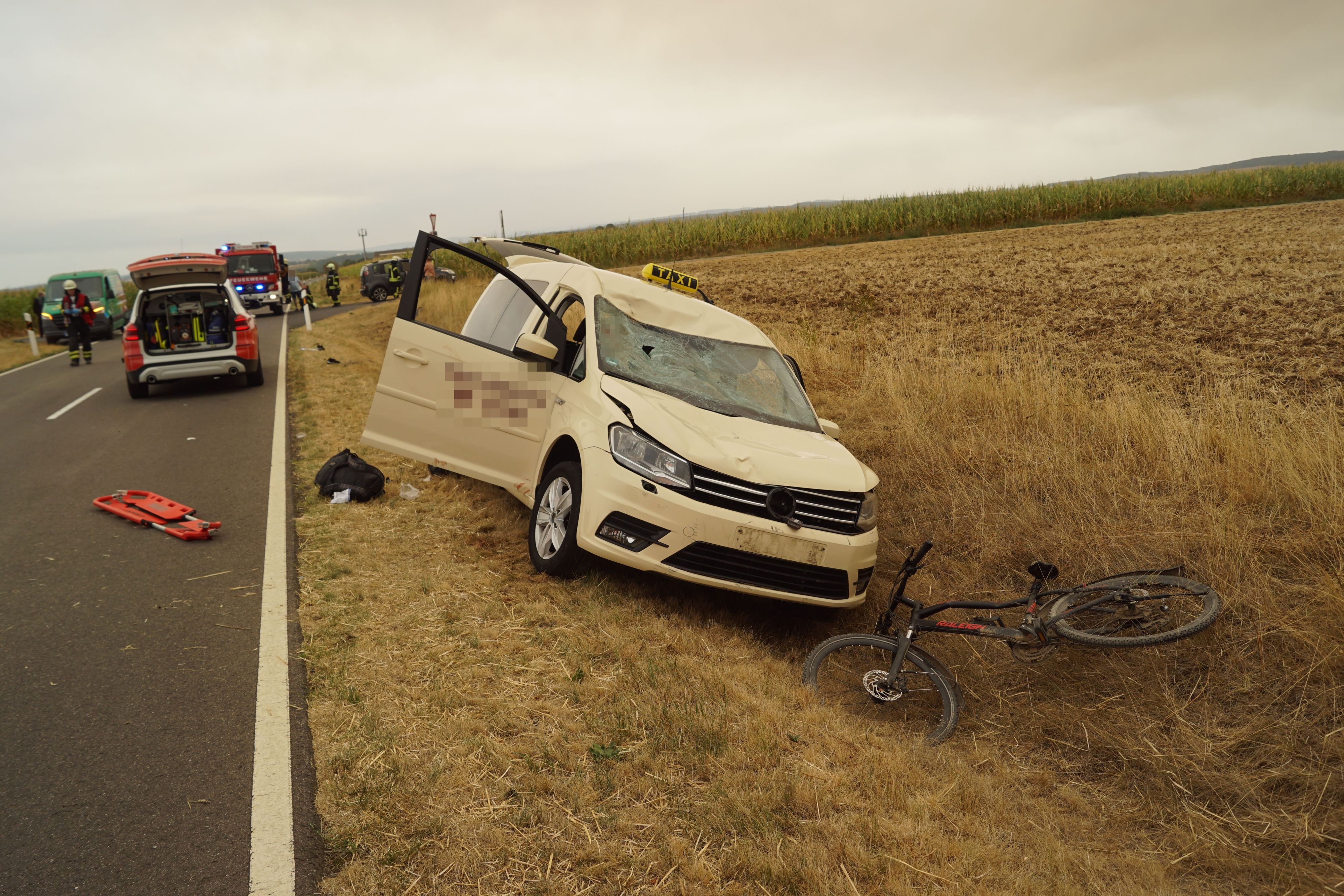 Ein zerbeultes Fahrrad liegt im Graben, ein Taxi mit Dellen in der Motorhaube steht dahinter ebenfalls im Graben.