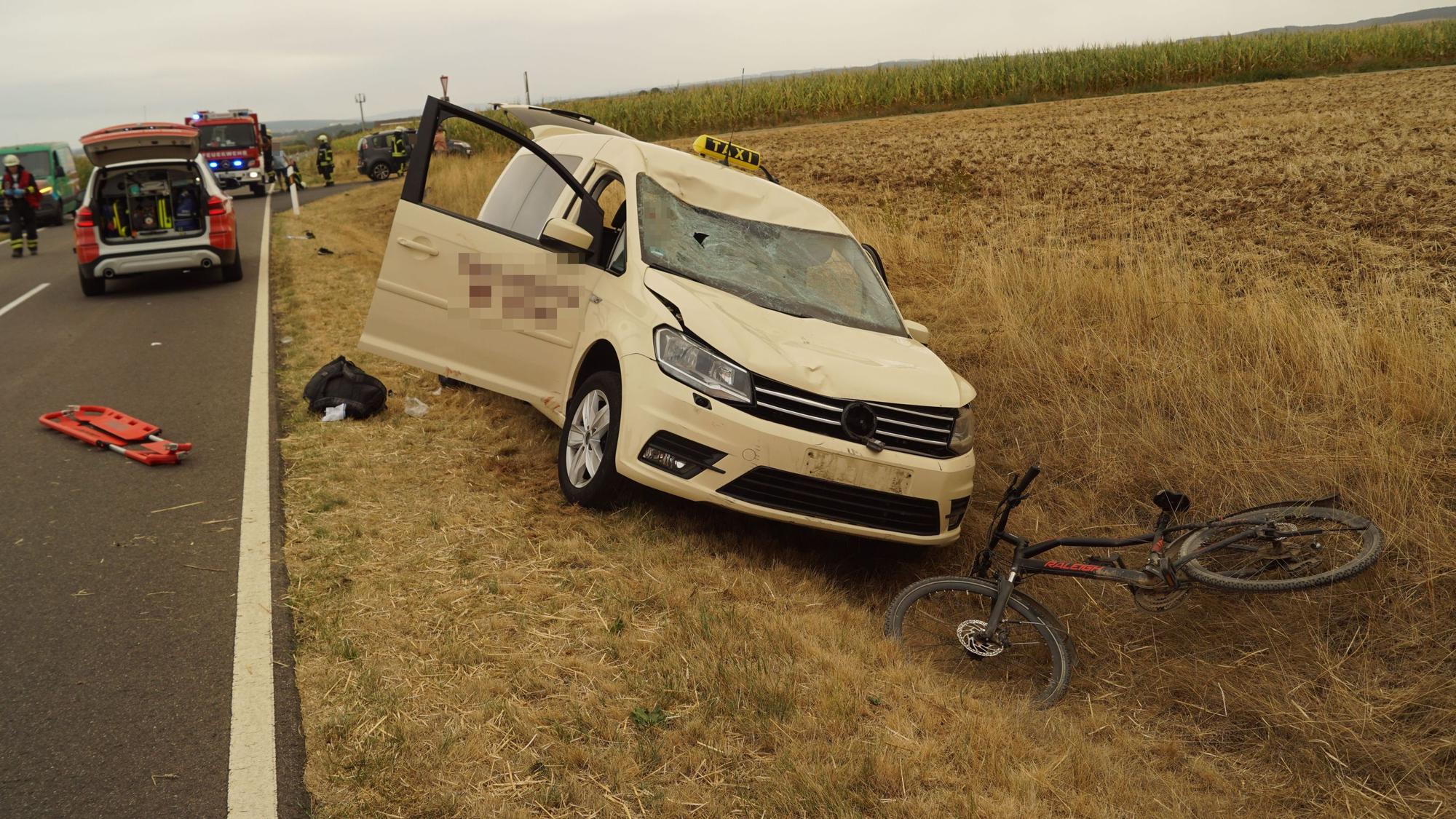 Ein zerbeultes Fahrrad liegt im Graben, ein Taxi mit Dellen in der Motorhaube steht dahinter ebenfalls im Graben.