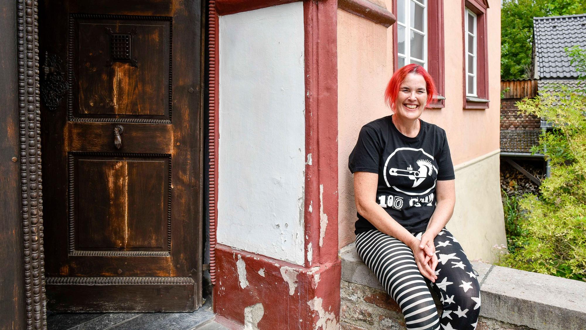 Eine Frau sitzt auf einer Mauer vor einem Haus.