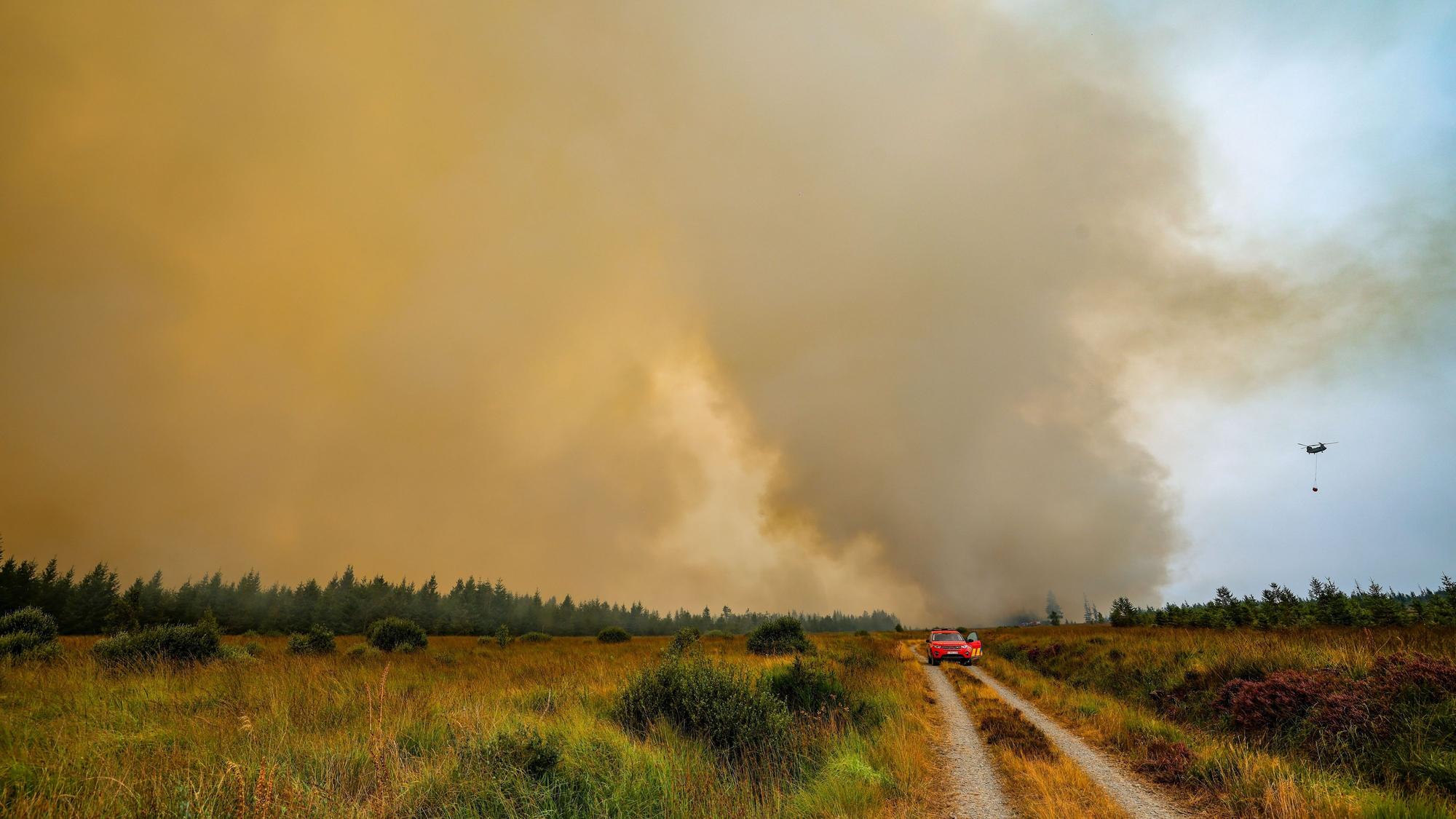 Die belgische Feuerwehr bekämpft den Brand in der Hochmoor- und Sumpflandschaft Hohe Venn unweit der deutschen Grenze. Gleichzeitig ist ein Chinook-Hubschrauber mit einem Wassersack zur Bekämpfung der Flammen im Einsatz.