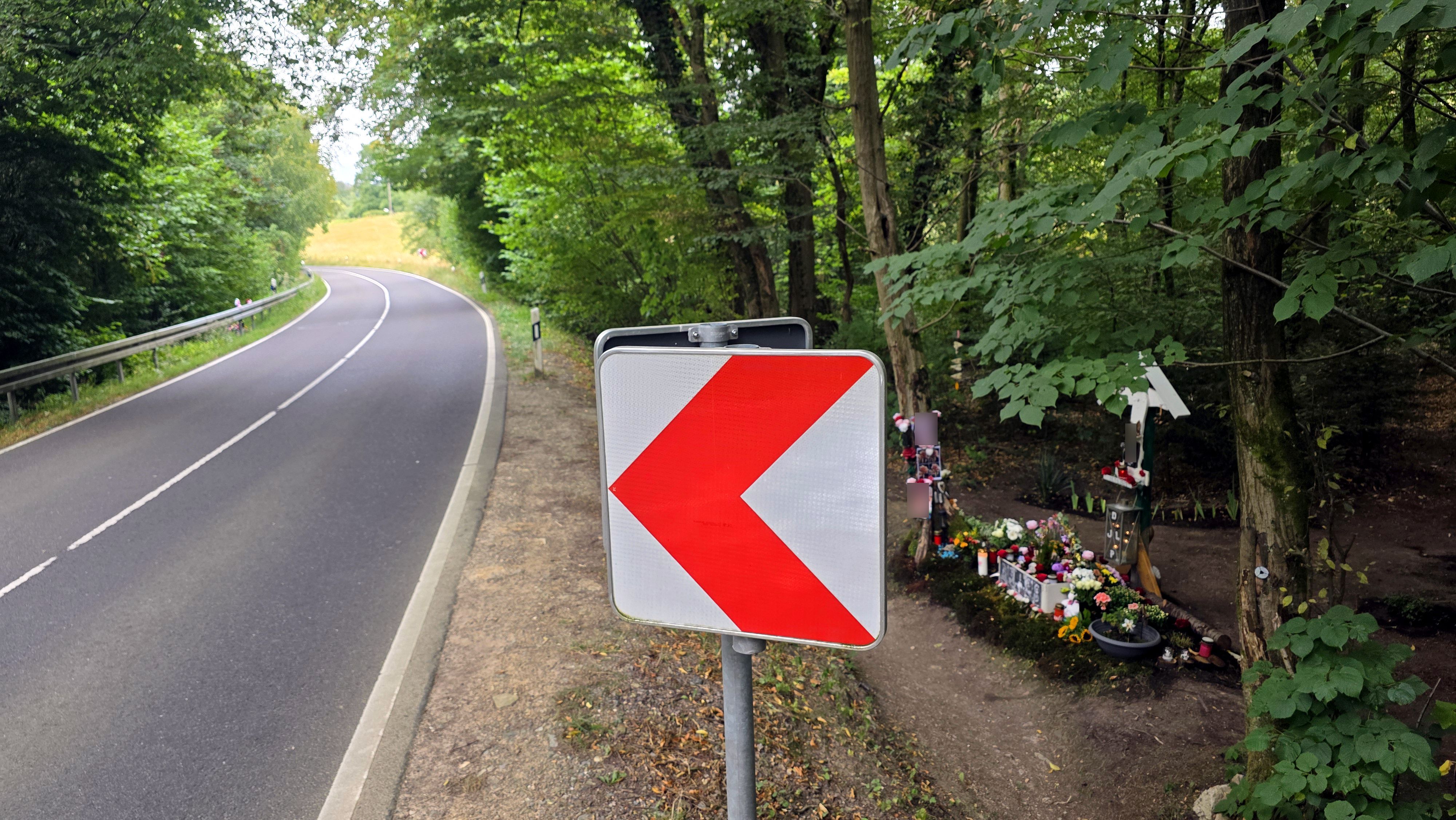 Eine Warntafel steht in einer Kurve der Dürschtalstraße. Im Graben neben der Straße ist eine Gedenkstätte für hier ums Leben gekommene Teenager zu sehen.