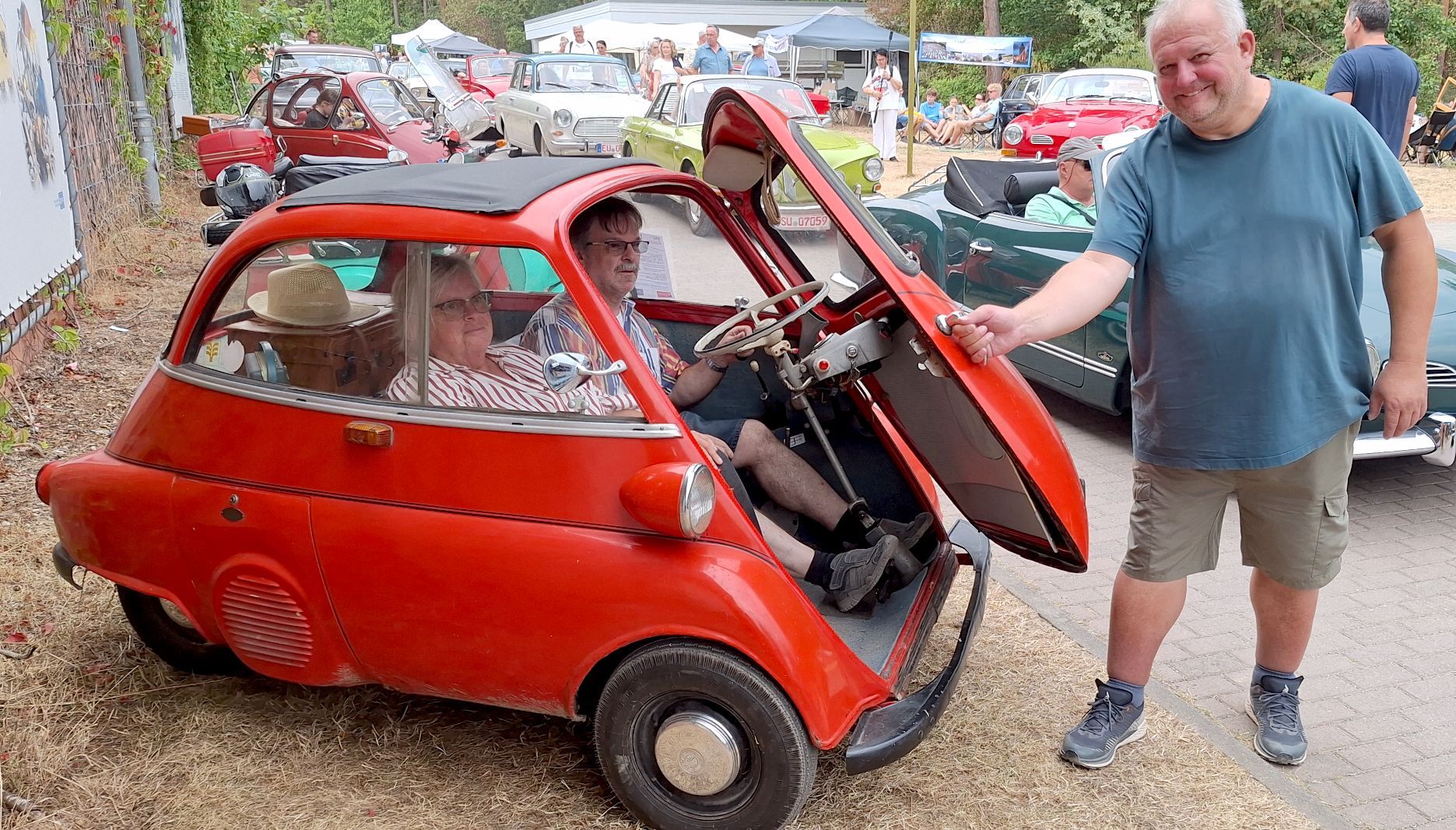 Ein Mann schließt die Klappe einer roten BMW Isetta, in der zwei Personen sitzen.