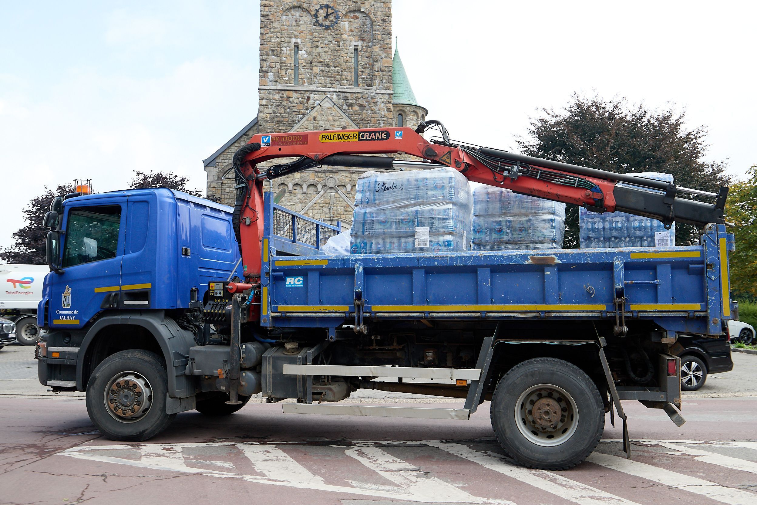 Auf einem blauen Lastwagen mit Ladekran befinden sich mehrere Paletten mit Wasserflaschen.